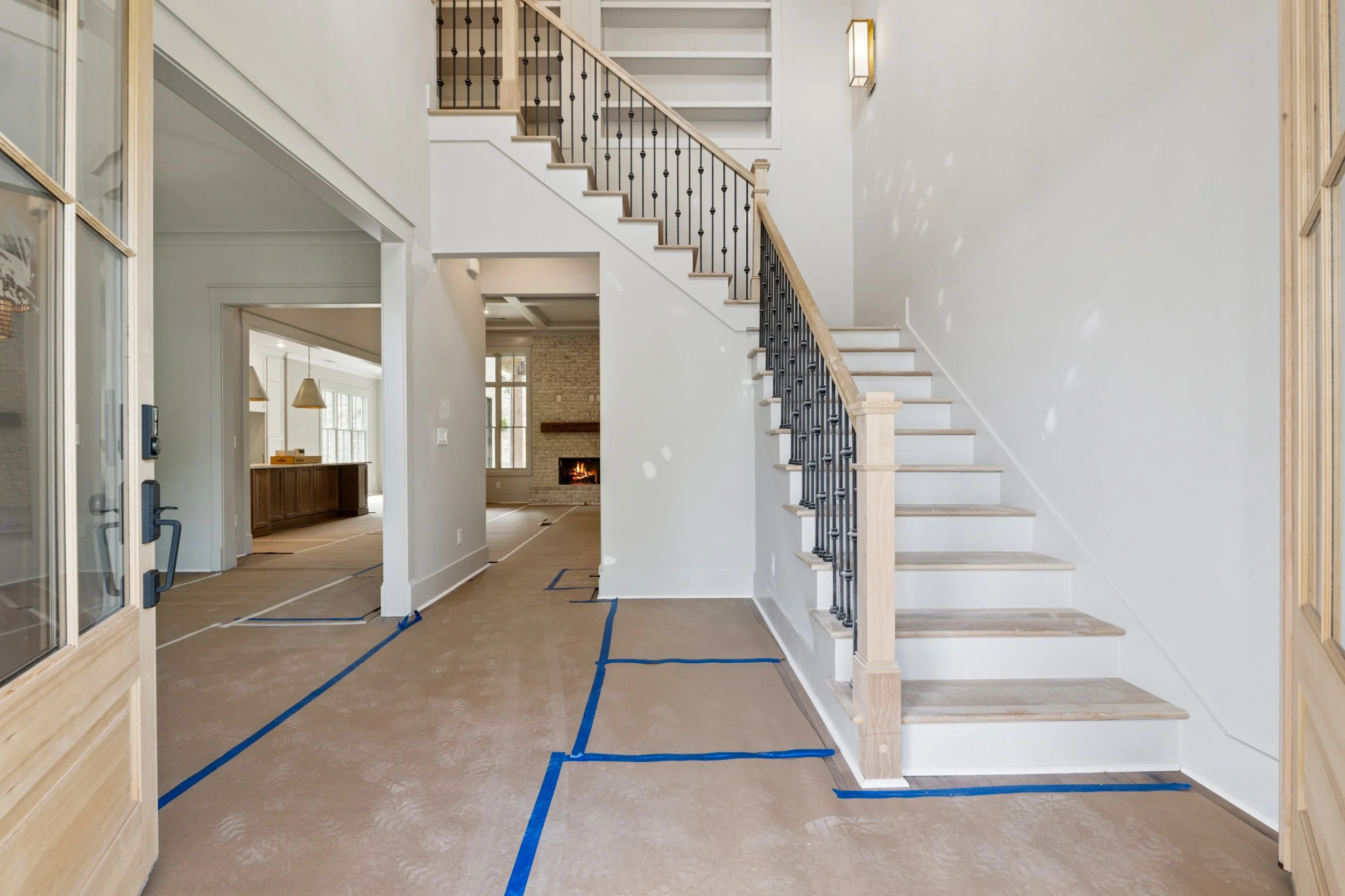 Interior of a house under renovation with a staircase, fireplace, and blue tape outlines on the floor.