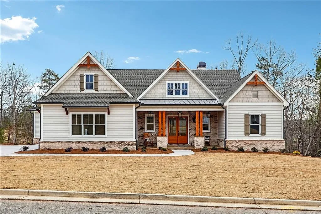 Front view of a new suburban house with a manicured lawn, brick and siding exterior, multiple gables, and a covered porch.