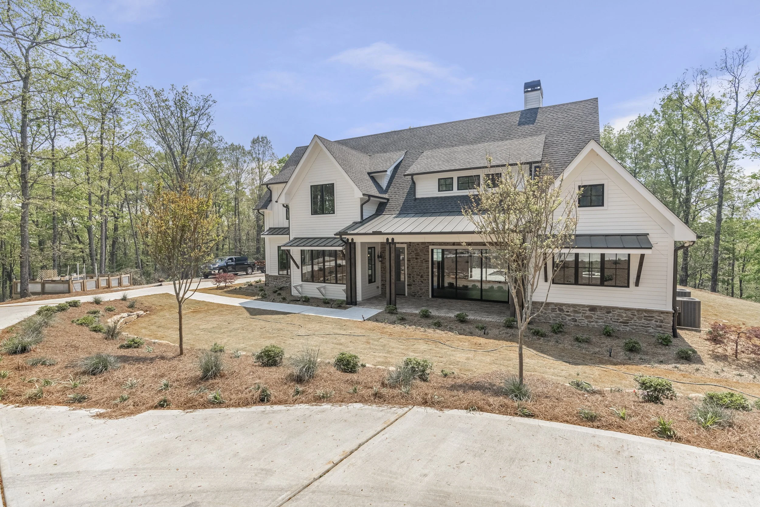 A modern two-story house with white siding, black window frames, and a gray roof surrounded by trees and a landscaped front yard.