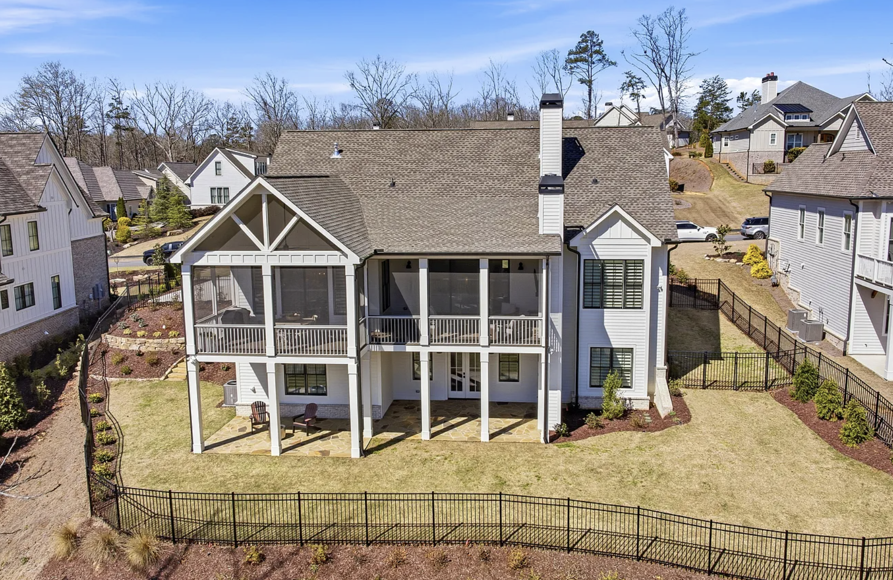 A modern two-story white house with a large backyard, screened-in porch, and multiple large windows, located in a suburban neighborhood with neighboring houses, trees, and a clear blue sky.