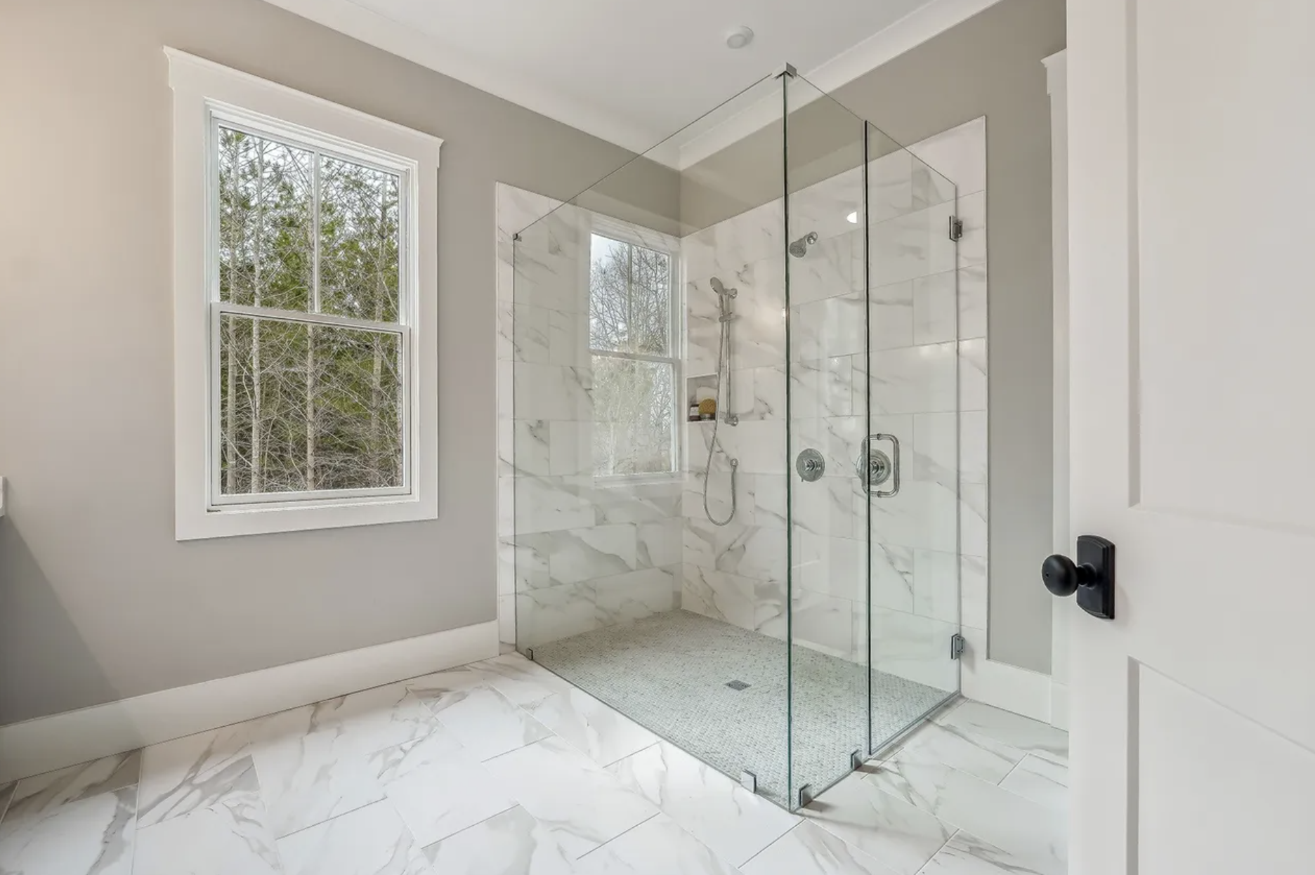 Modern bathroom with large window, marble tiles, and glass shower enclosure.