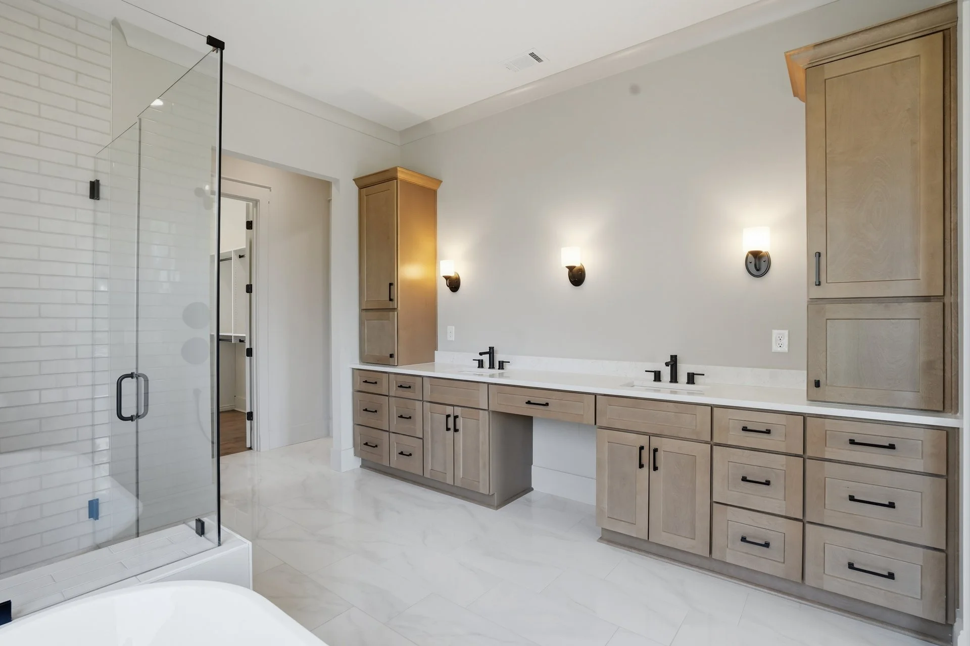 Modern bathroom with double vanity, light wood cabinets, black fixtures, and a glass shower enclosure.