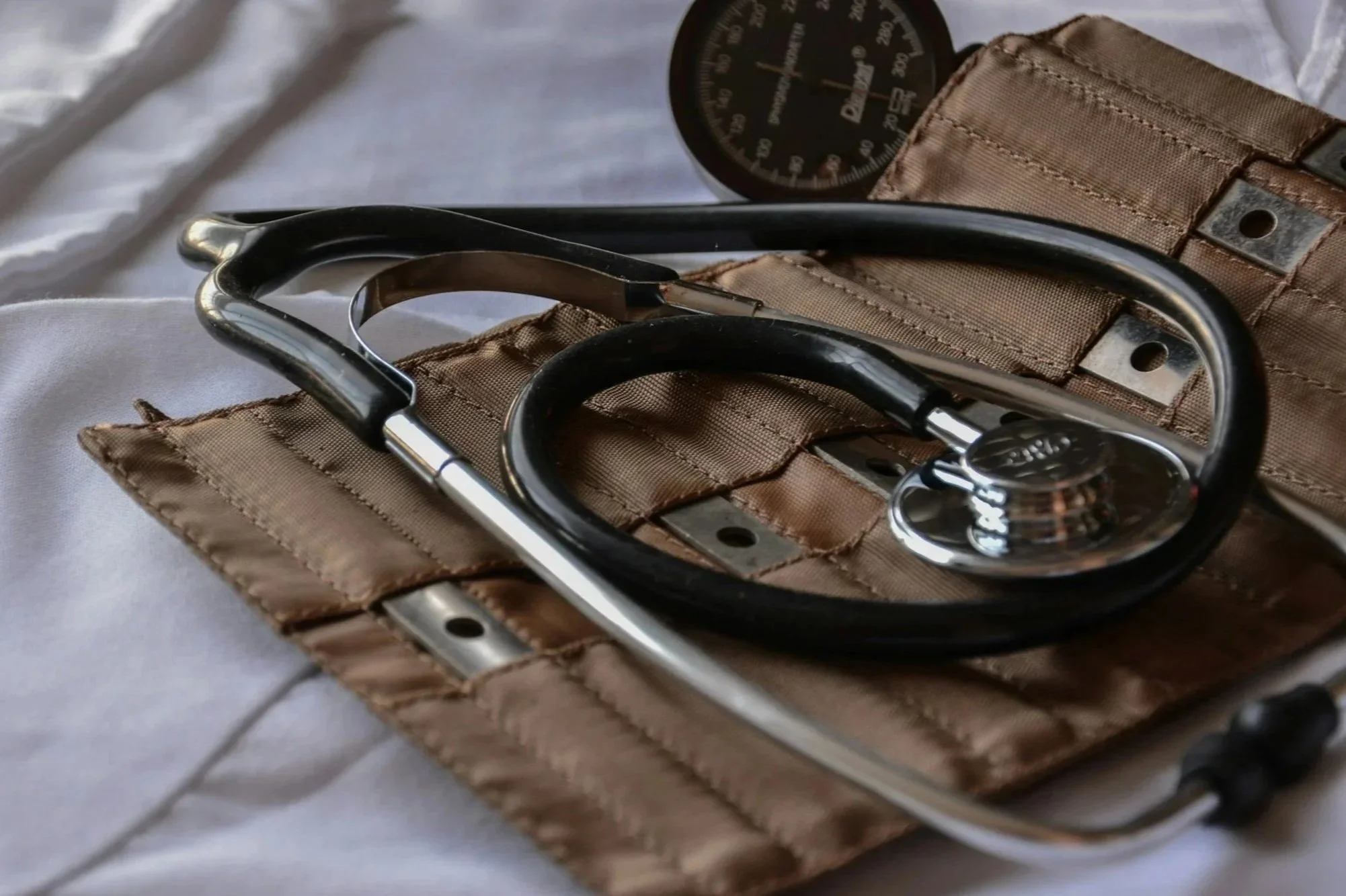 A pair of black stethoscopes are placed on a brown fabric pocket organizer, with a black sphygmomanometer gauge in the background.