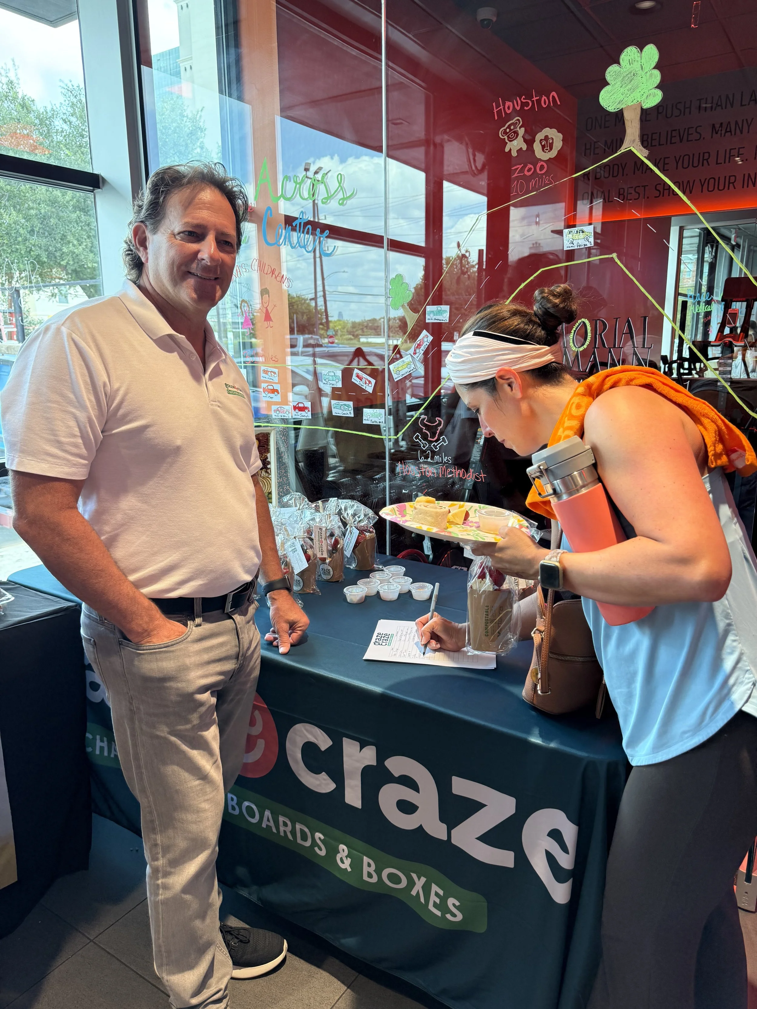 A man standing next to a woman signing a clipboard at a booth with a sign that reads 'Craigslist Boards & Boxes' and a colorful display behind them.