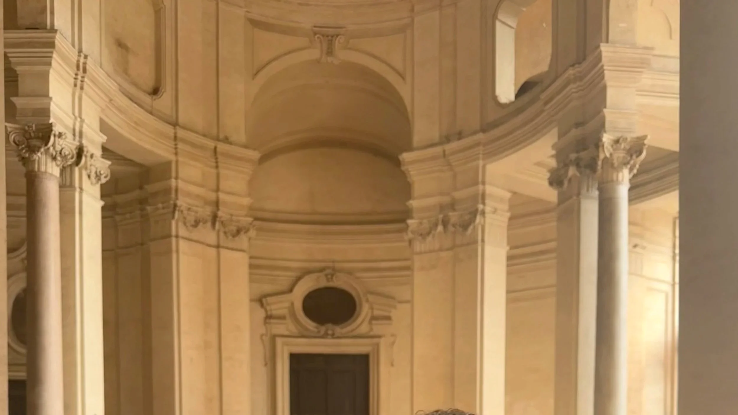 Interior view of a historic building with tall columns, ornate architectural details, and a rounded ceiling.