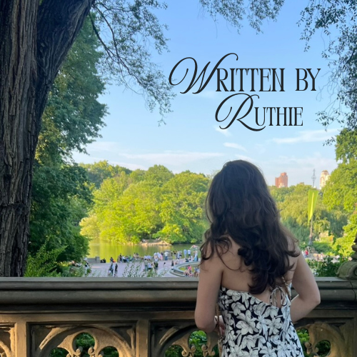 A woman with long dark hair, wearing a black and white floral dress, standing on a balcony overlooking a park with lush green trees and a river, under a clear blue sky, with the text 'Written by Ruthie' in the top right.