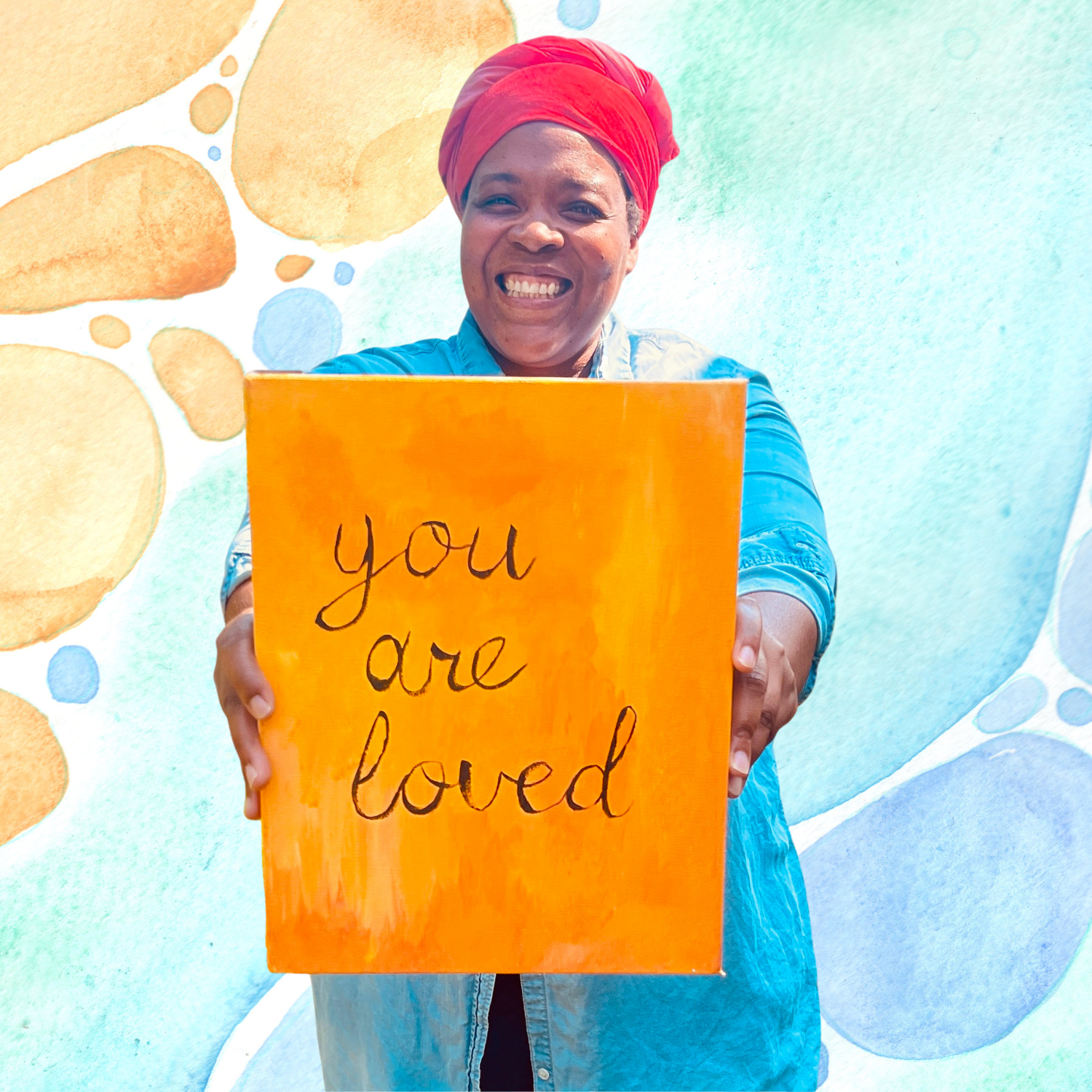 Bellamy Shoffner - writer and artist - holds a canvas that says you are loved in script