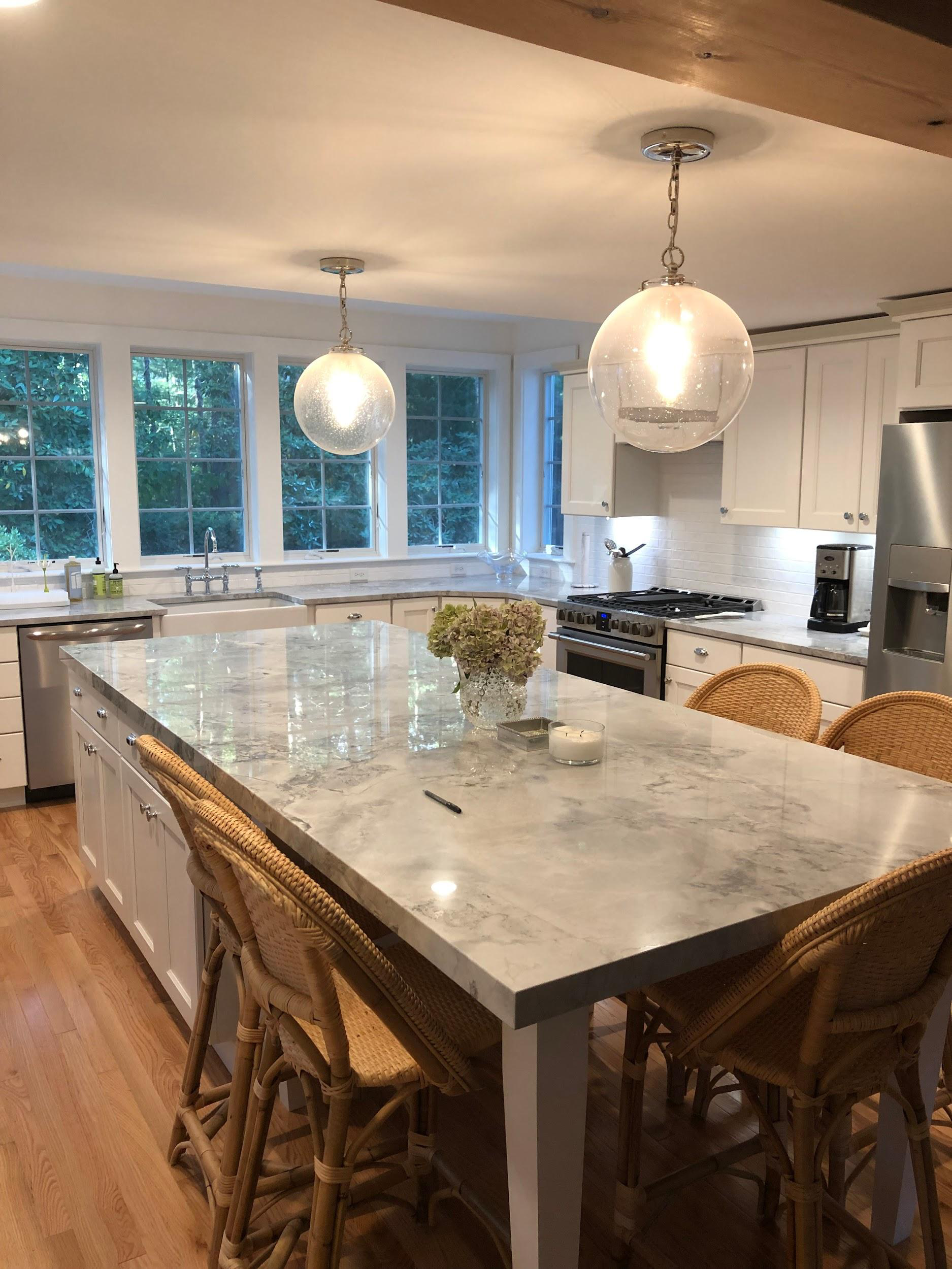A kitchen with white cabinets, a marble countertop island, and two pendant lights hanging from the ceiling. Mastercraft Building & Remodeling in Massachusetts offers kitchen remodels.