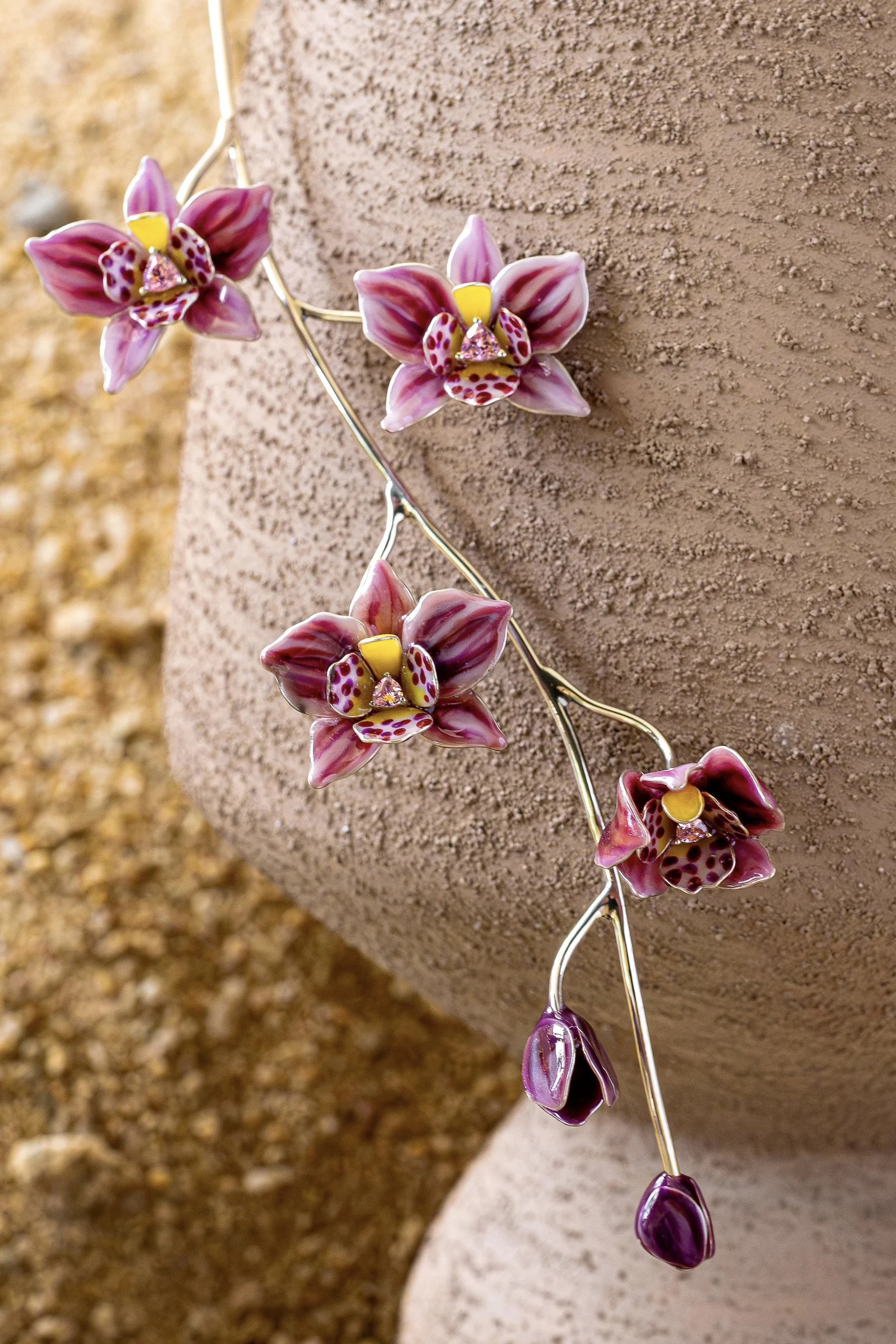 Close-up of a decorative necklace with purple orchid-shaped flowers, yellow centers, and pink dotted patterns, draped over a textured beige and brown surface.