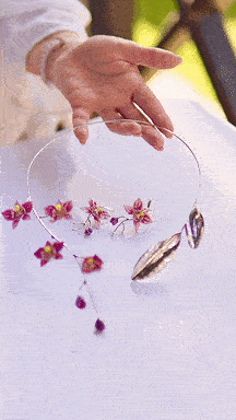 A person handling a clear circular object with pink flowers and a fish inside, possibly a fish trap or decorative display, on a white surface.
