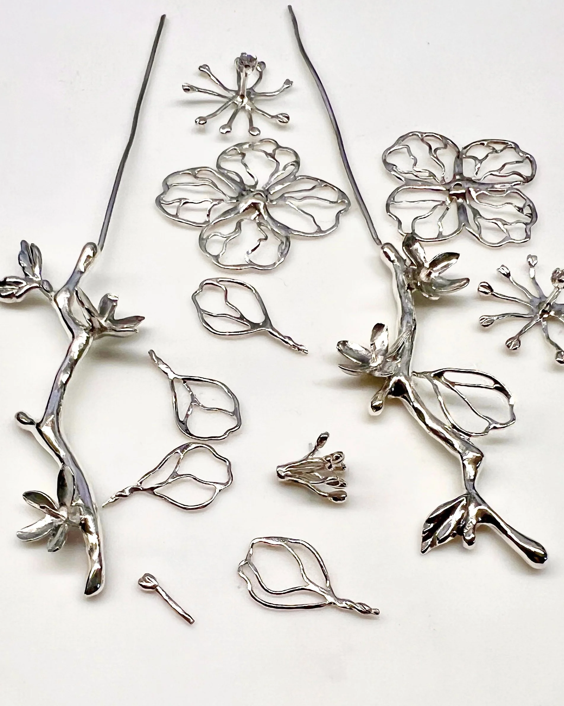 Silver metal decorative flower and branch jewelry pieces on a white background.
