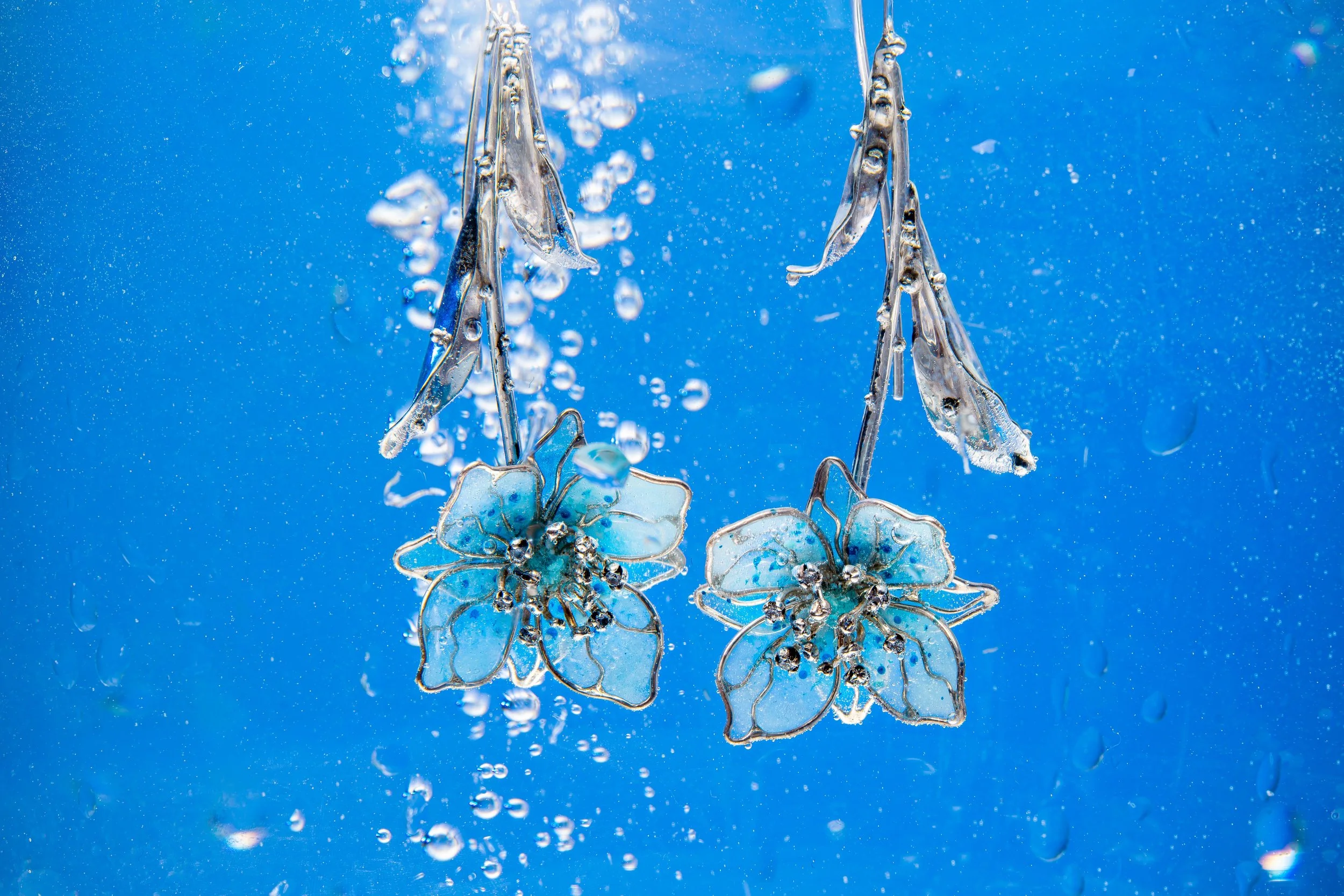 Close-up view of sparkling snowflake-shaped jewelry with blue background and water bubbles.