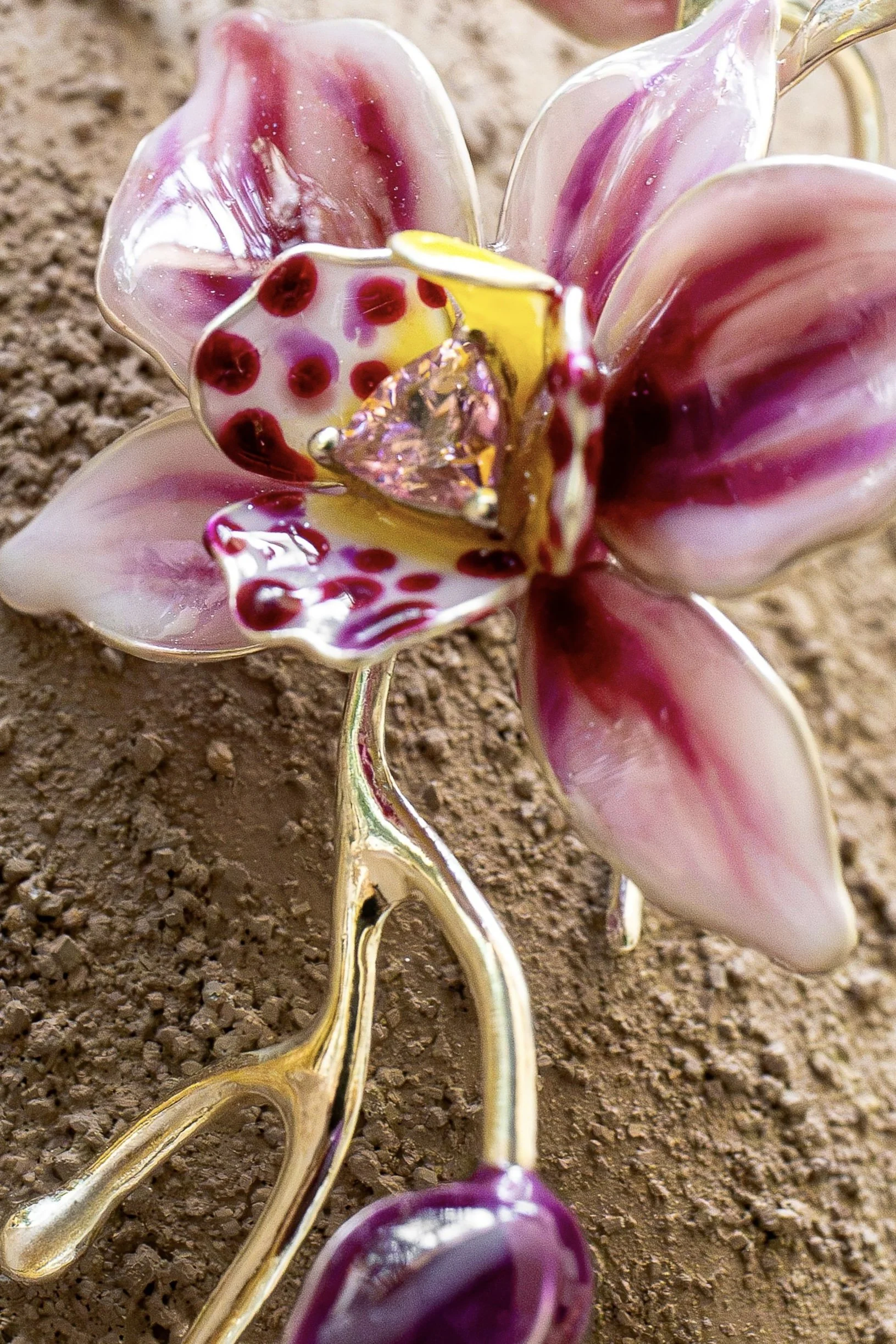 Close-up of a decorative flower-shaped object with pink, purple, white, and gold colors, placed on a textured brown surface.