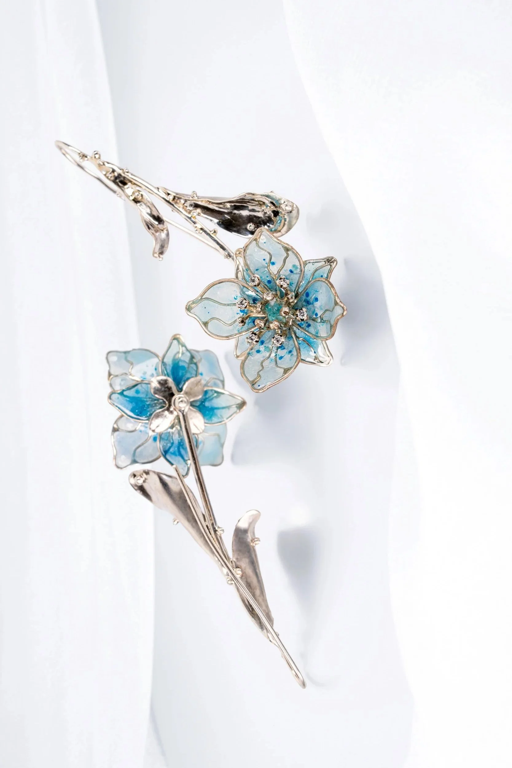 Silver floral brooch with blue and clear gemstones on a white background.