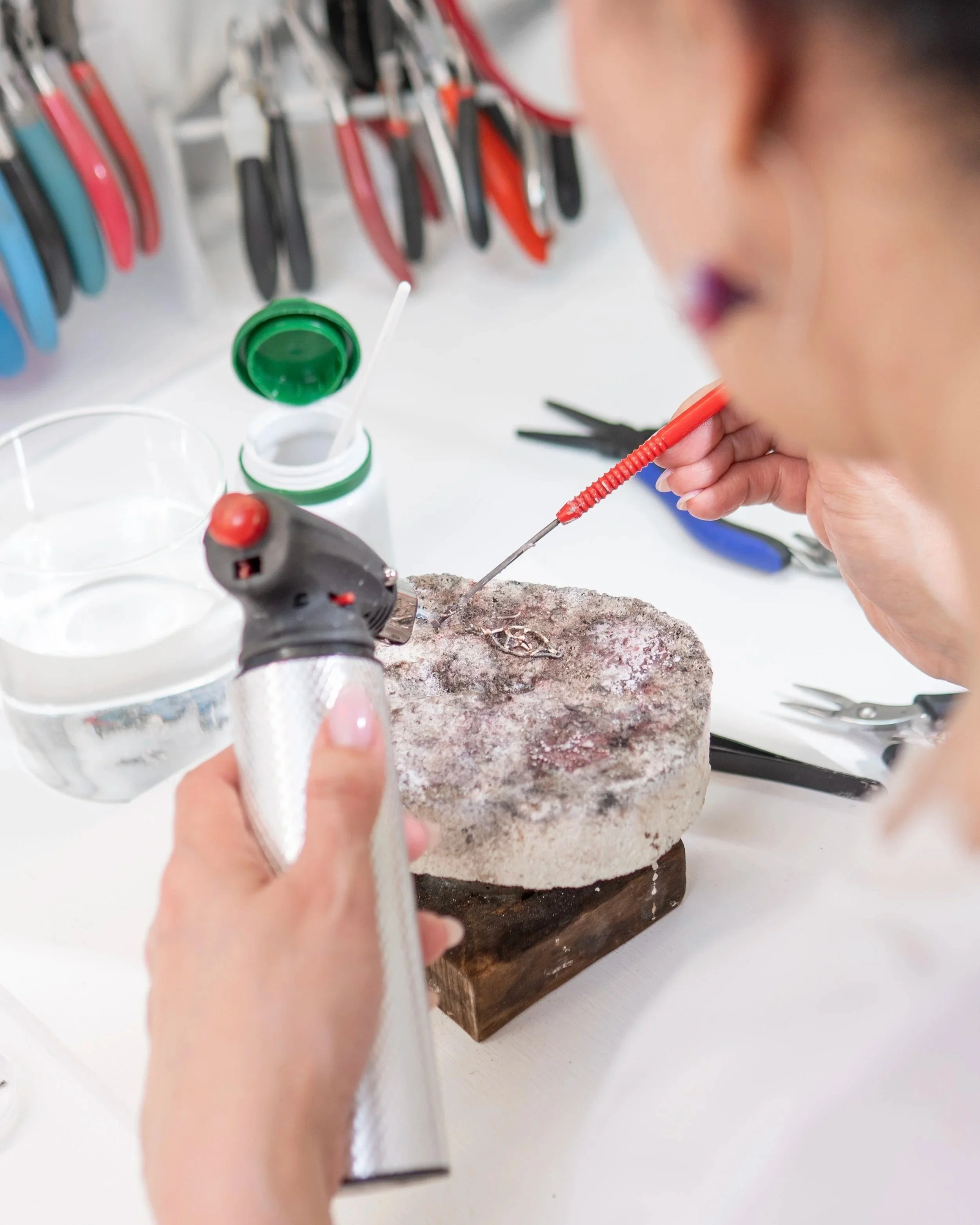 Person using a soldering iron on a piece of material at a workbench surrounded by tools and supplies.