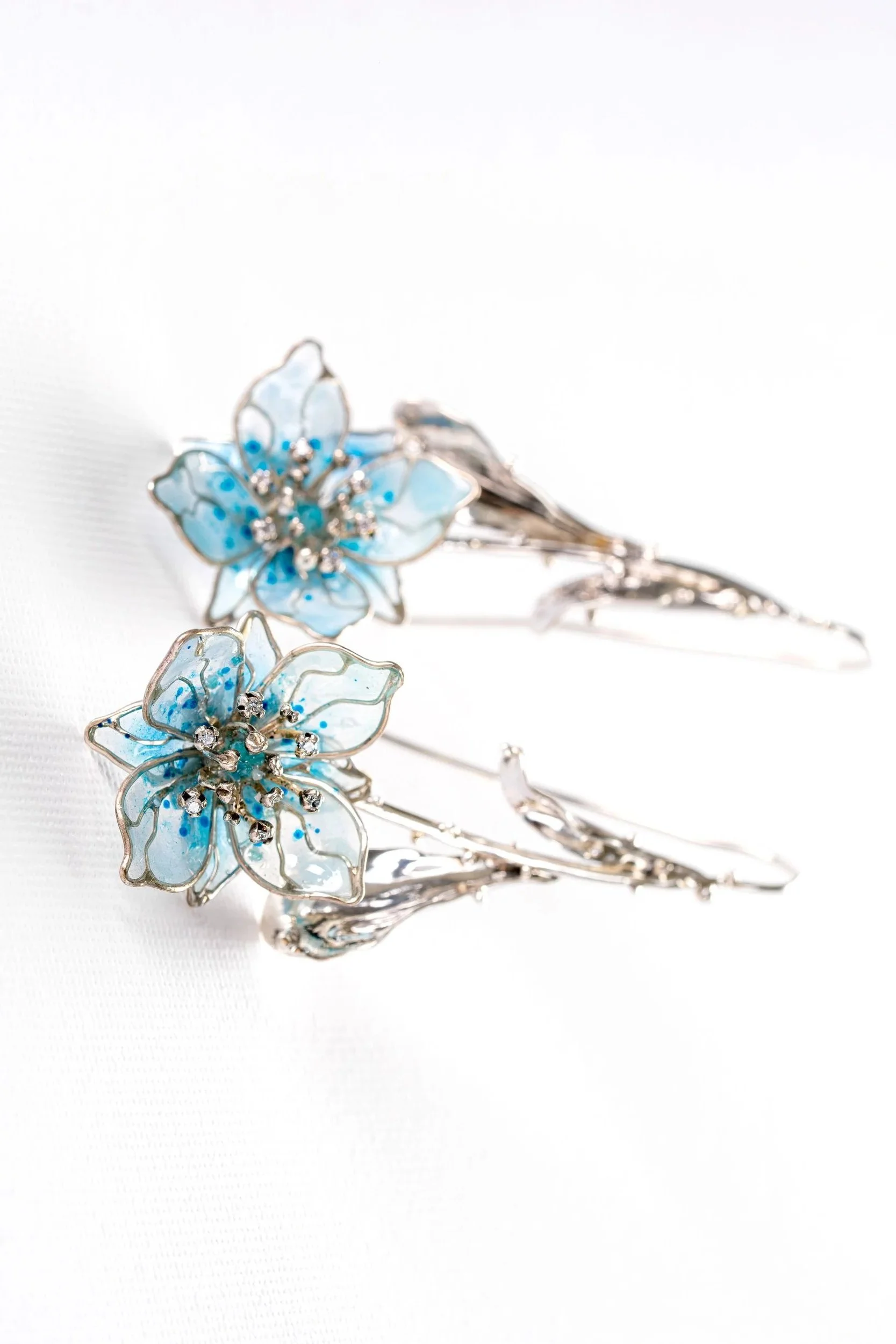 Silver hair accessories shaped like blue flowers with rhinestone centers on a white background.