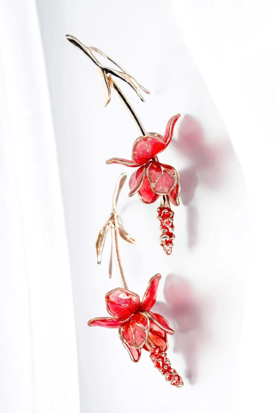 Jewelry piece designed as a flower and plant motif with red and gold accents, against a white background.