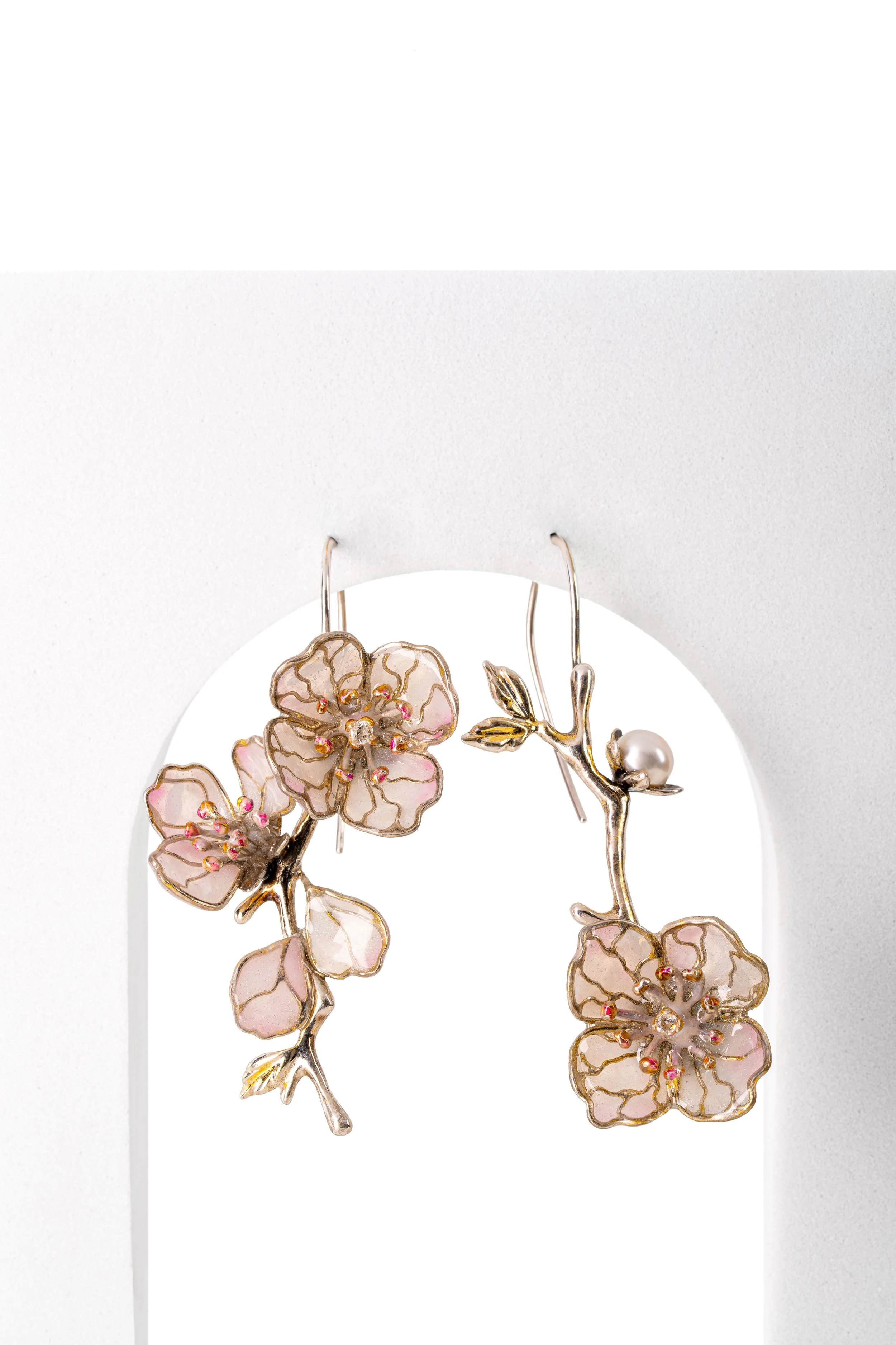 Elegant earrings with pink and gold floral design, featuring small gemstones and a pearl, displayed on a white backdrop.