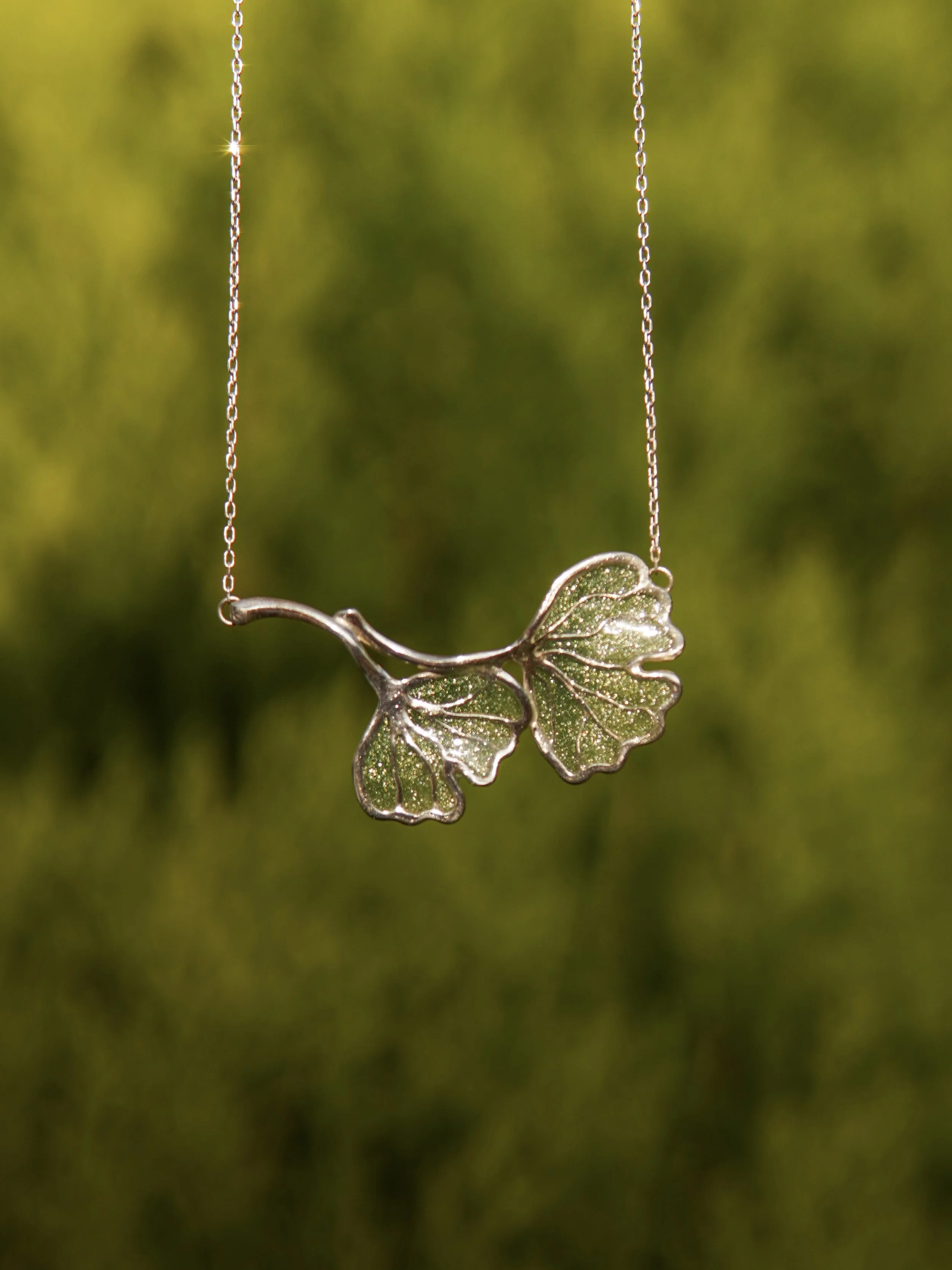 A silver necklace with a butterfly-shaped pendant hanging against a blurred green background.