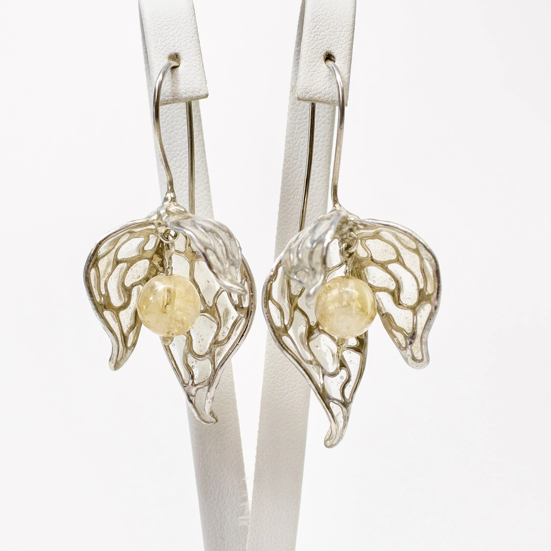Close-up of a pair of earrings with a intricate gold filigree design, hanging on white earring holders.