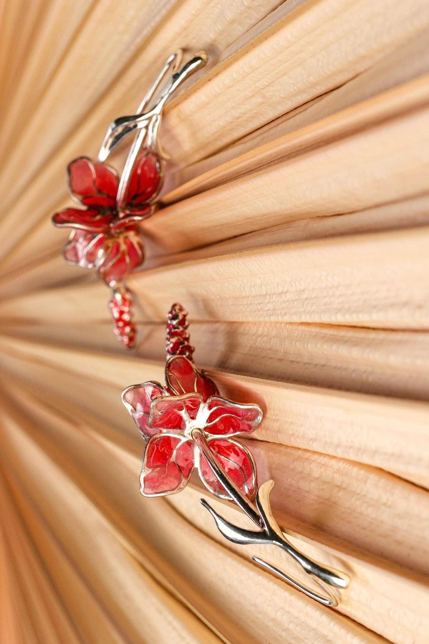 A metal flower-shaped hair clip with red petals attached to a wooden background.