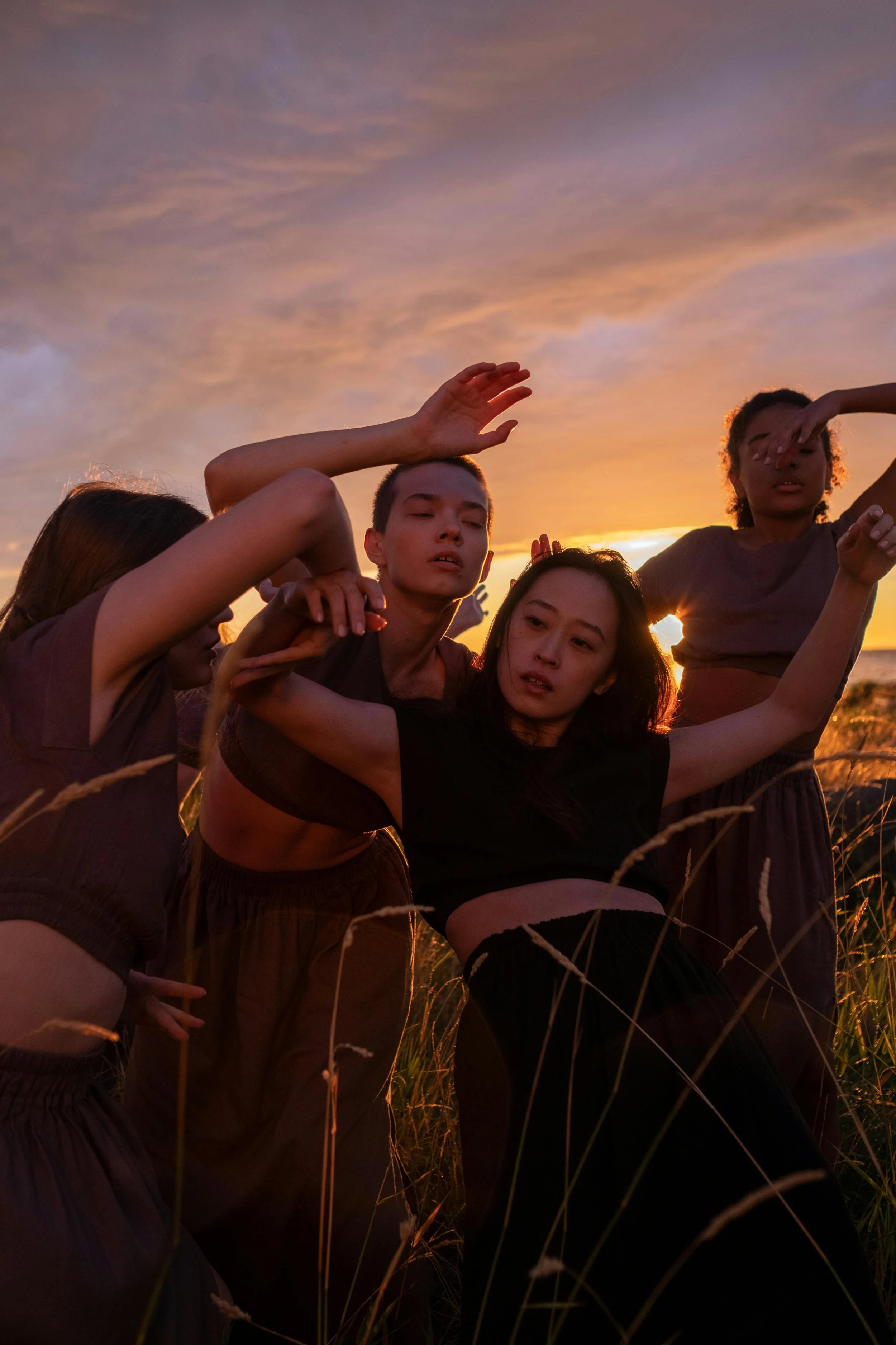 Groupe de personnes dansant librement dans un champ au coucher du soleil