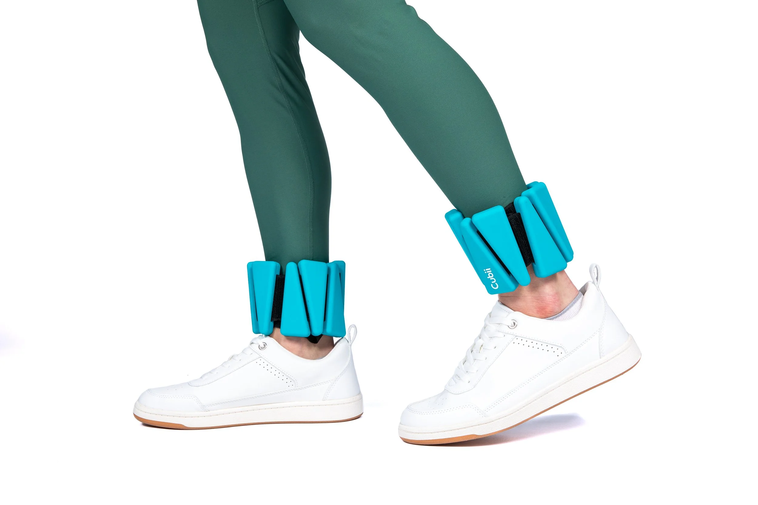 Person wearing white sneakers and green athletic pants with blue ankle weights on both legs.