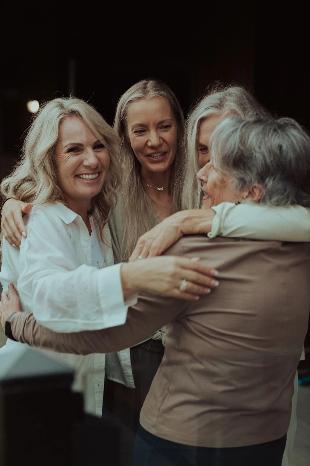 Four women embracing each other joyfully, smiling, sharing a heartfelt moment.