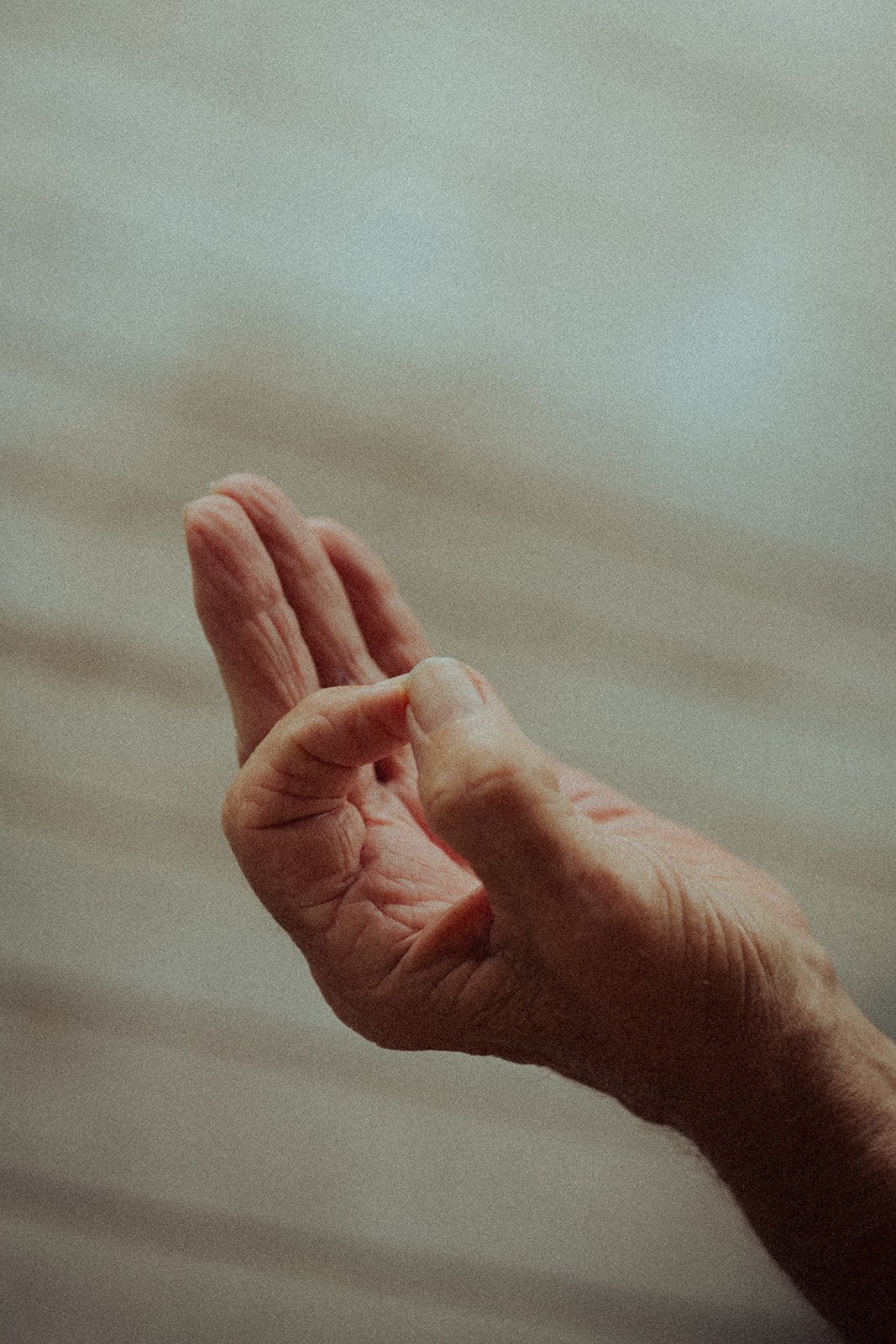 Close-up of an elderly person's hand making a gesture with thumb and index finger touching, and other fingers extended.