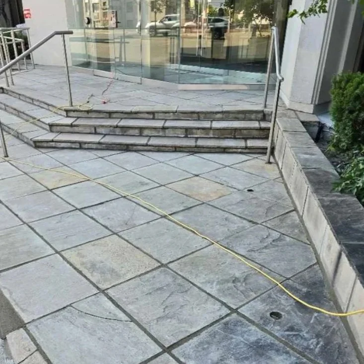 The steps leading to an entrance with a glass railing and a tiled outdoor area, with construction materials and a yellow cable on the ground.
