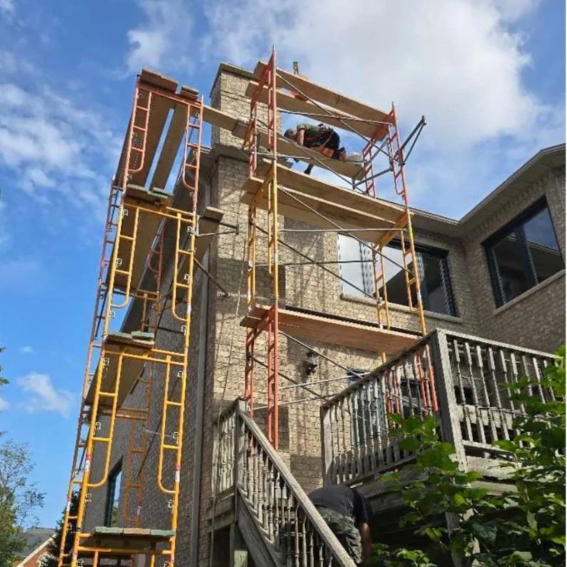 Construction worker on scaffolding working on the exterior of a brick house during daytime.