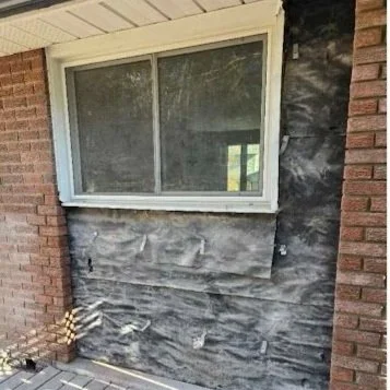 Exterior wall with brick on both sides and house wrap underneath a window, with some siding temporarily removed.