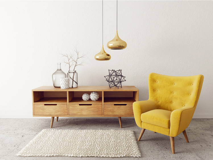 Living room decor featuring a yellow armchair, wooden sideboard with decorative vases, a geometric sculpture, a dried branch, and hanging gold pendant lights on a white wall, with a cream area rug on the light gray floor.