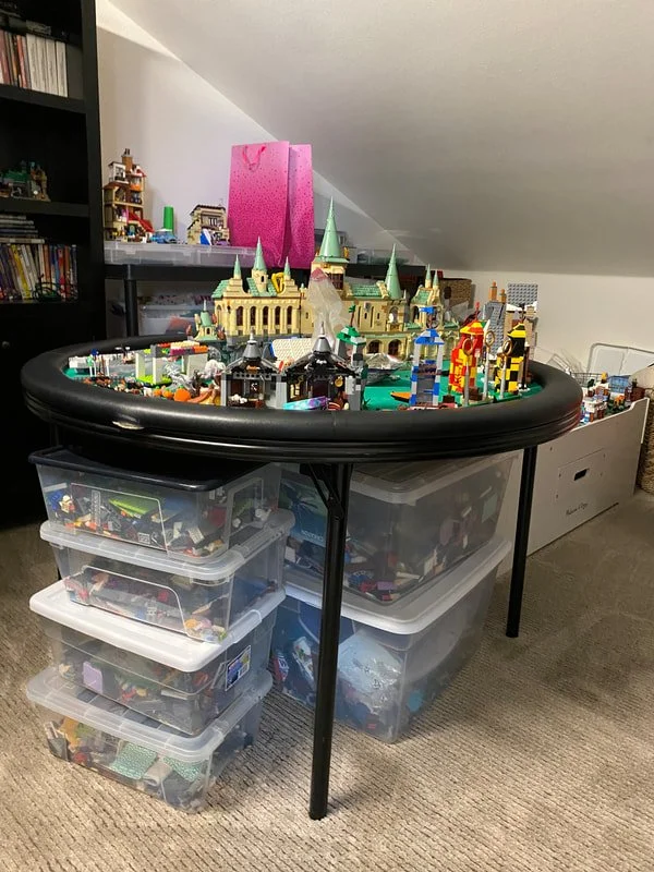 Lego cityscape on a round table with storage bins underneath, featuring various colorful Lego structures including a castle with green spires and detailed buildings.