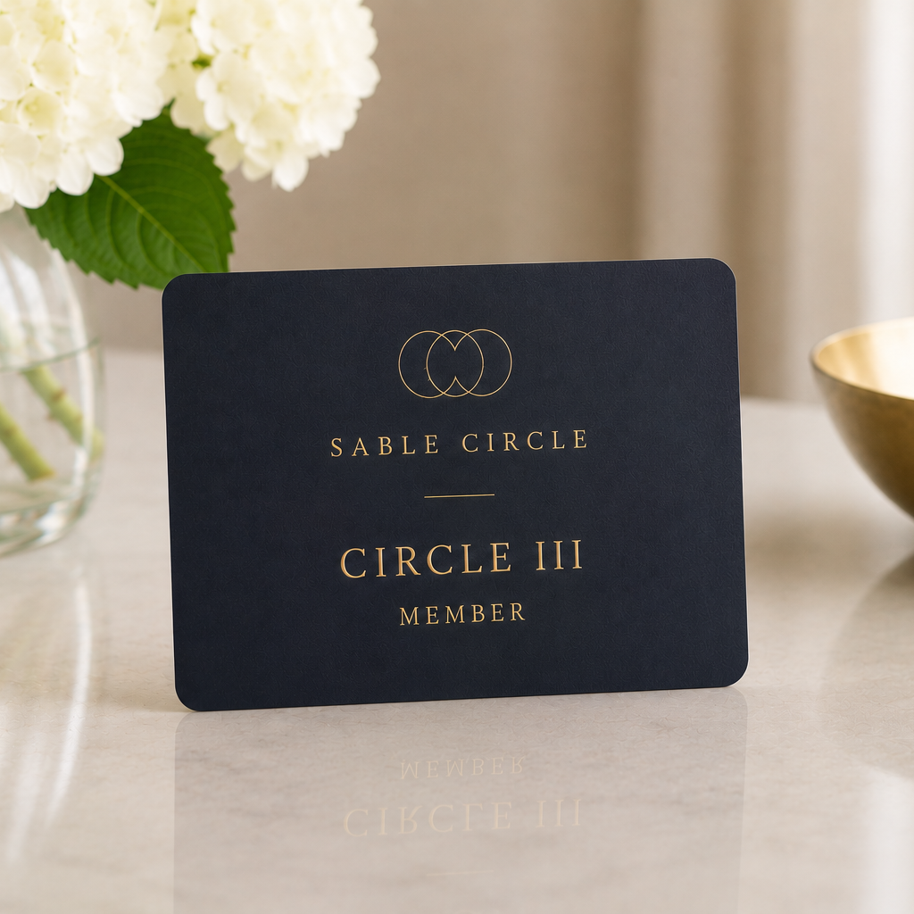 A dark blue card with gold lettering on a marble surface, with white hydrangea flowers in a glass vase to the left and a gold bowl to the right.