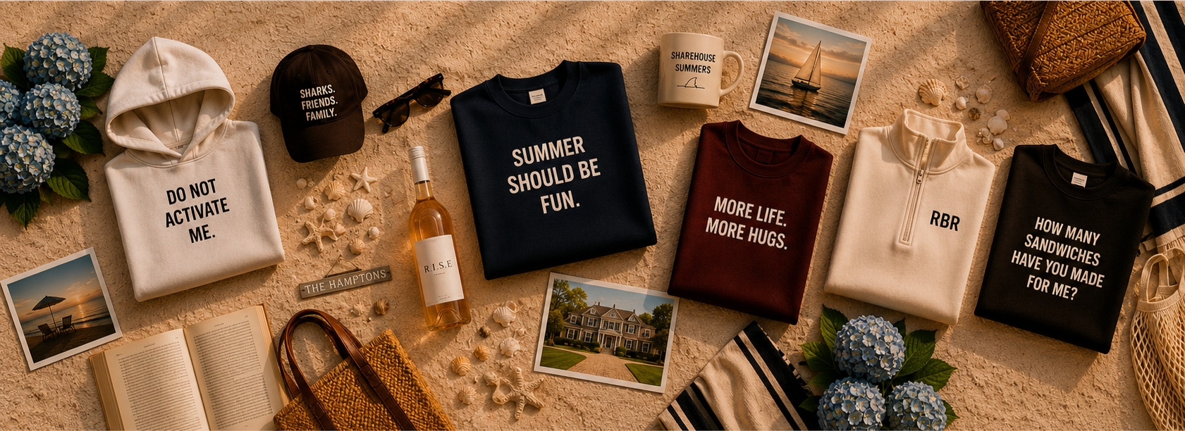 Flat lay of summer vacation items on sandy surface, including folded sweatshirts with printed slogans, a baseball cap, sunglasses, a bottle of rosé wine, printed photographs, seashells, a mug, and flowers.