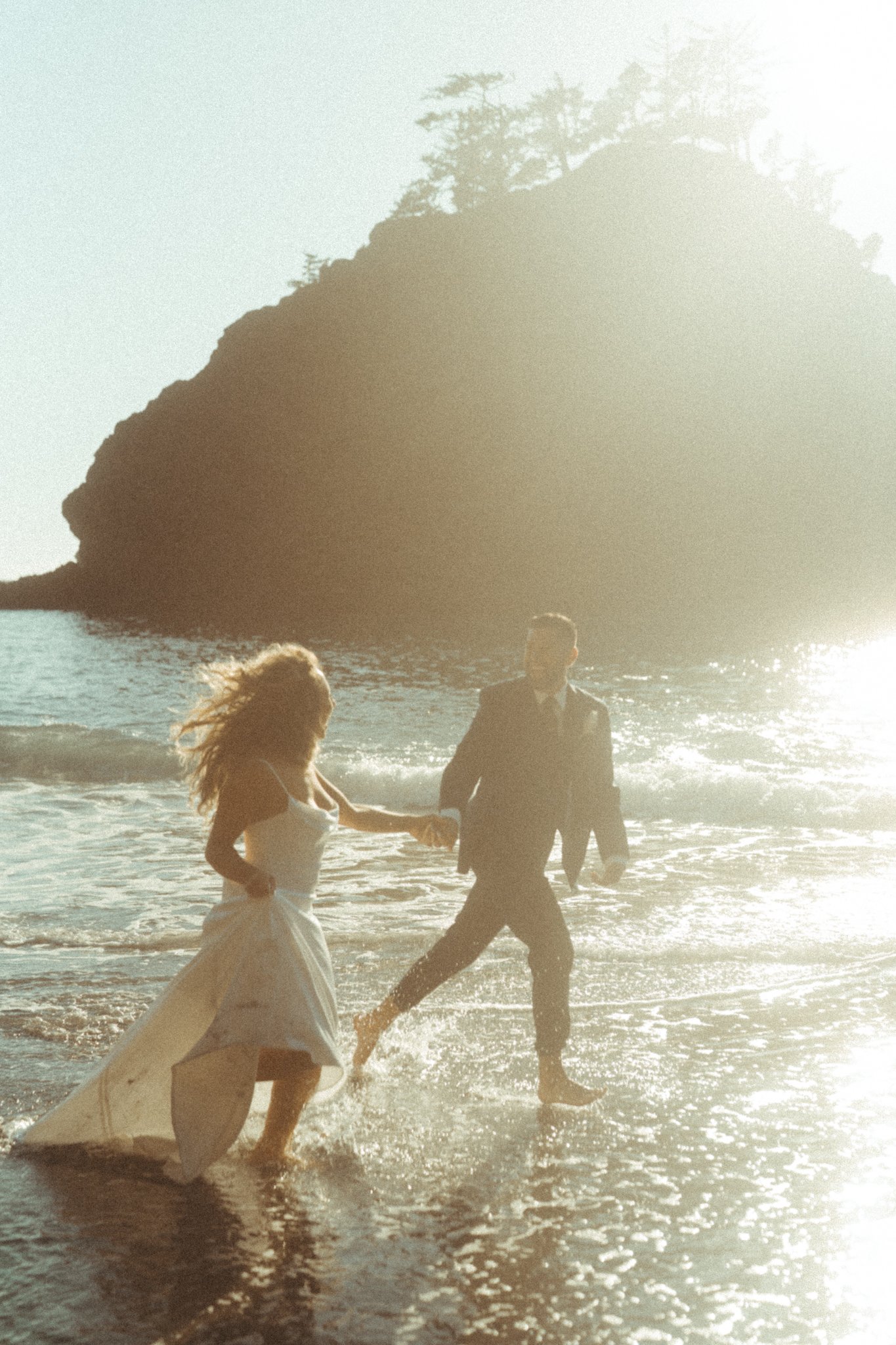 Bride and groom running through the ocean during a romantic beach wedding photography session.