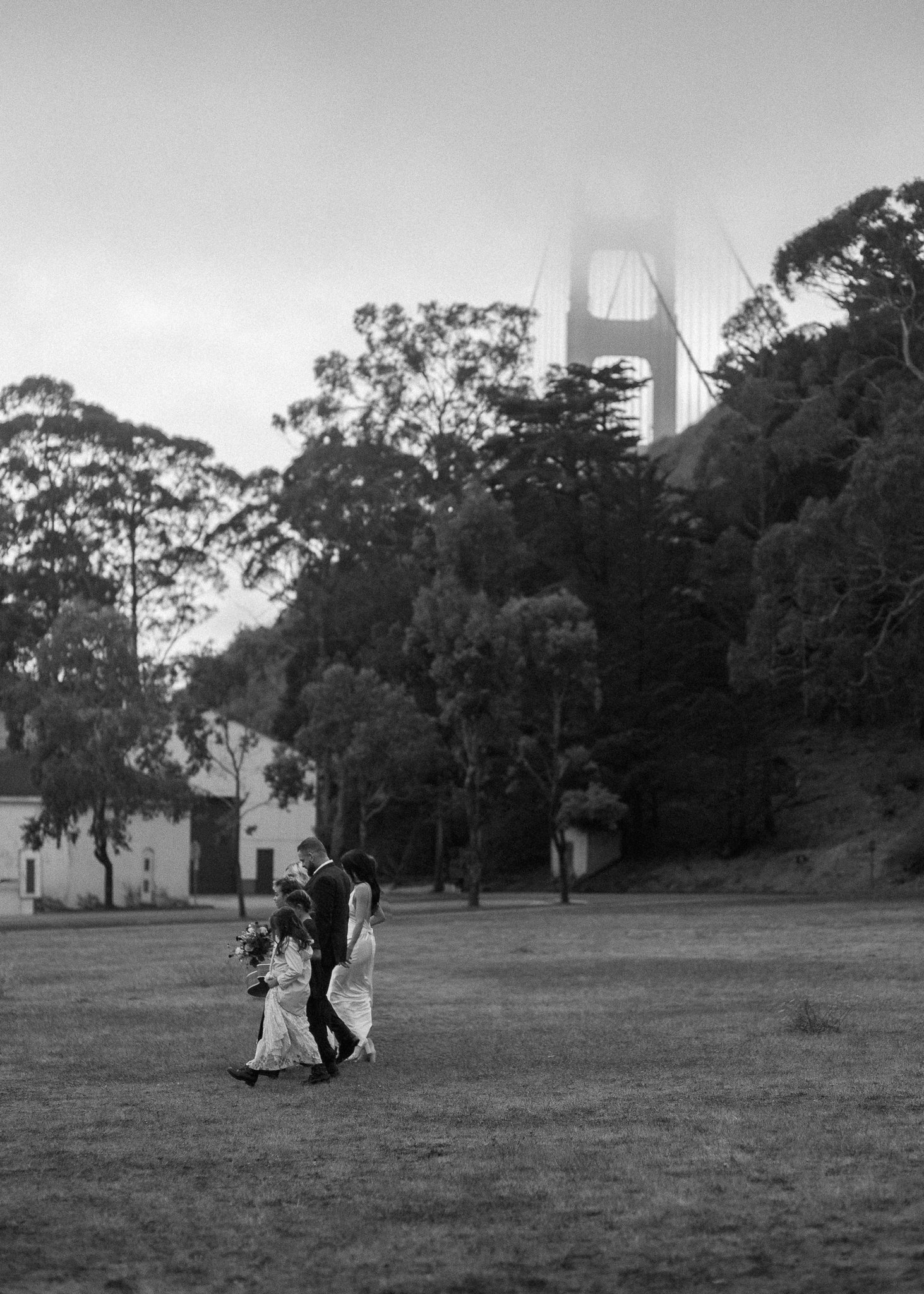 Bride and groom walking across a grassy field with the Golden Gate Bridge in the background during a San Francisco wedding.