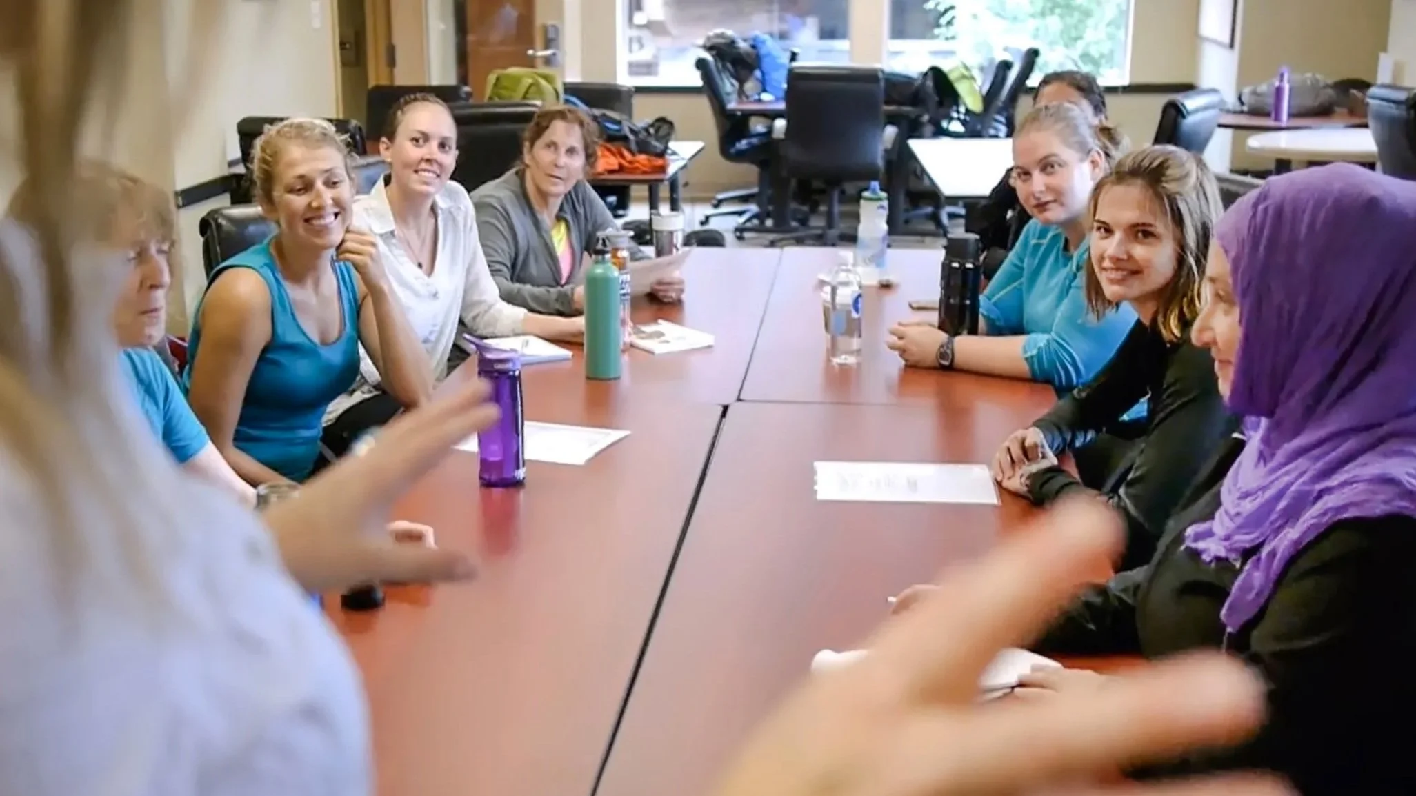 A group of women and girls sitting around a conference table in a meeting room, engaging in a conversation or discussion.