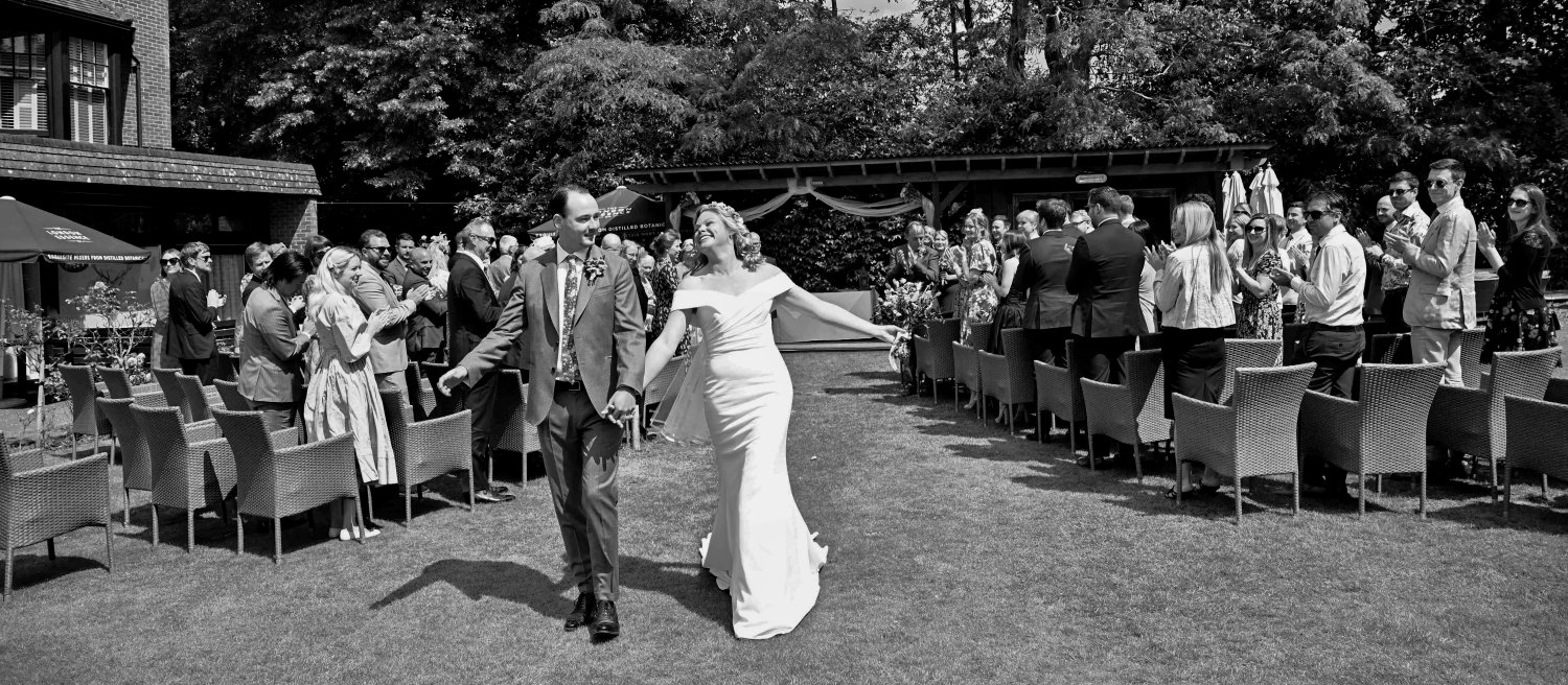 Bride and groom dancing back down the aisle as Mr & Mrs at an outdoor summer wedding ceremony — candid documentary wedding photography by Tasha Boorman, Nottinghamshire