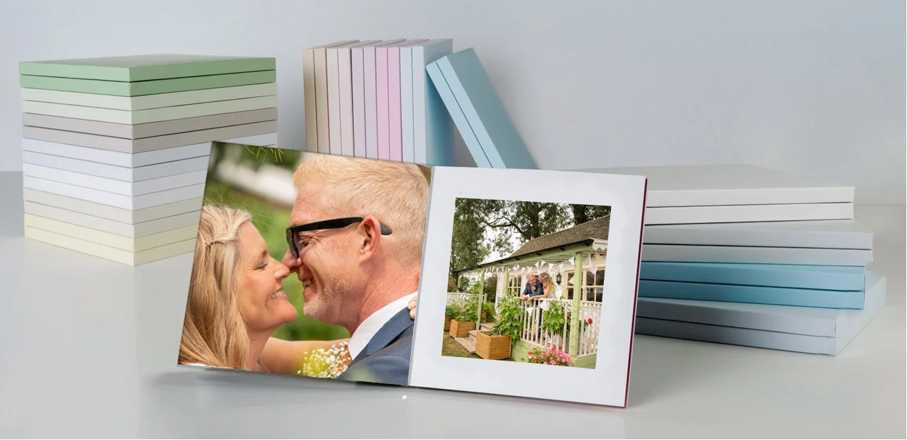 Open photo album displaying a couple smiling and a porch with two people sitting on it, with stacks of color-coordinated books in the background.