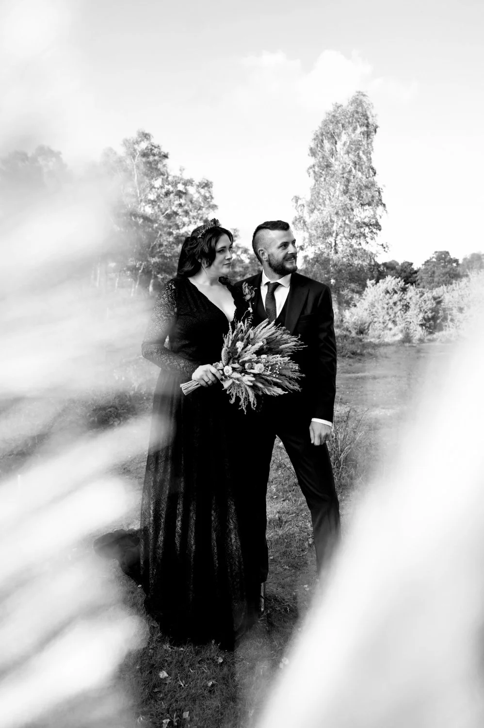 Alternative gothic bride in black wedding dress and groom framed through natural foliage in Nottinghamshire woodland — creative wedding portrait by Tasha Boorman, Nottinghamshire wedding photographer