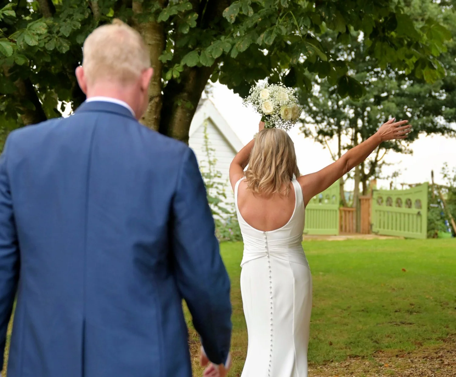 Bride and groom making their entrance at outdoor farm wedding, bride with arm outstretched holding bouquet, candid documentary wedding photography Leicestershire farm wedding venue