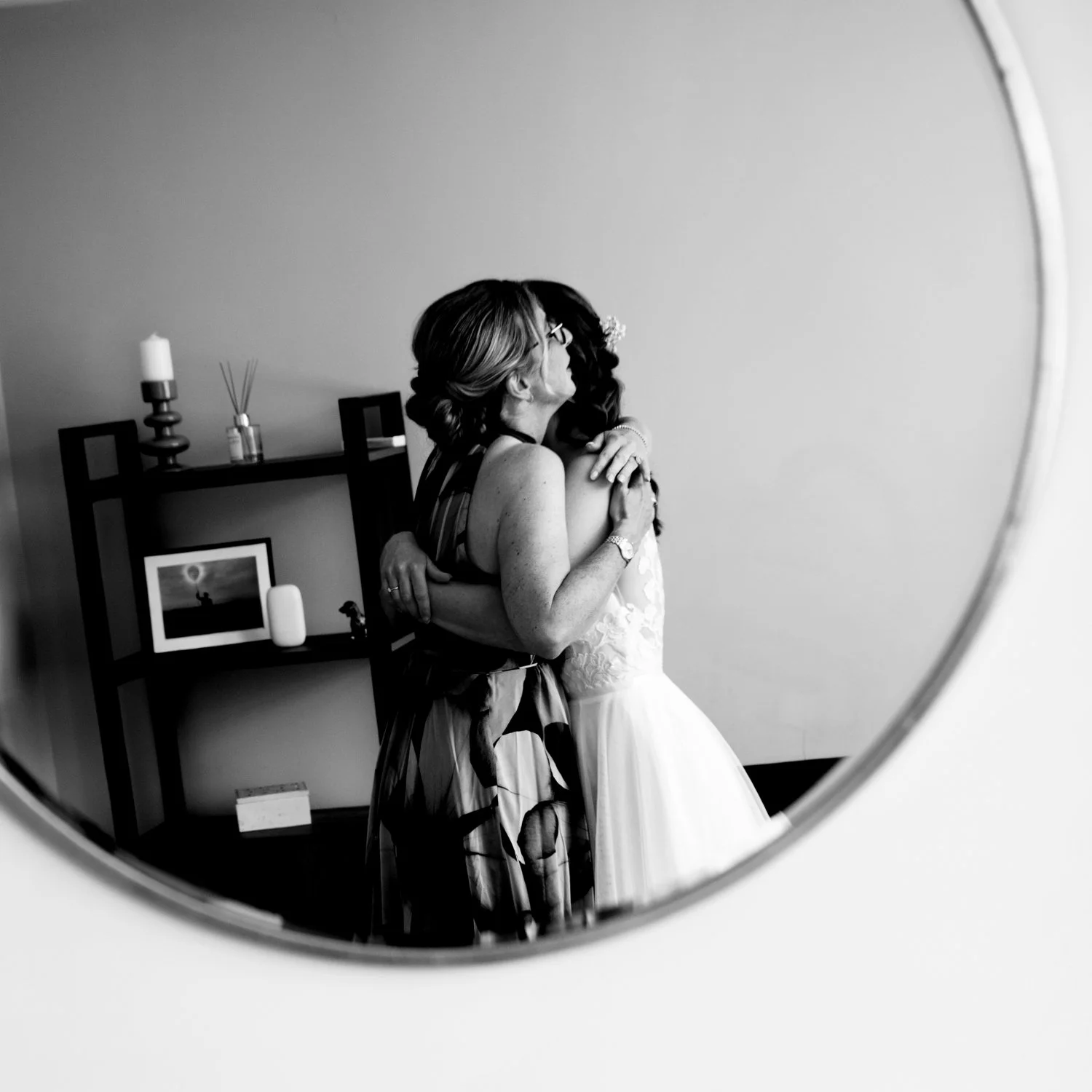 Mother and bride sharing an emotional embrace reflected in a round mirror during wedding morning preparations — creative documentary wedding photography by Tasha Boorman, Nottinghamshire wedding photographer