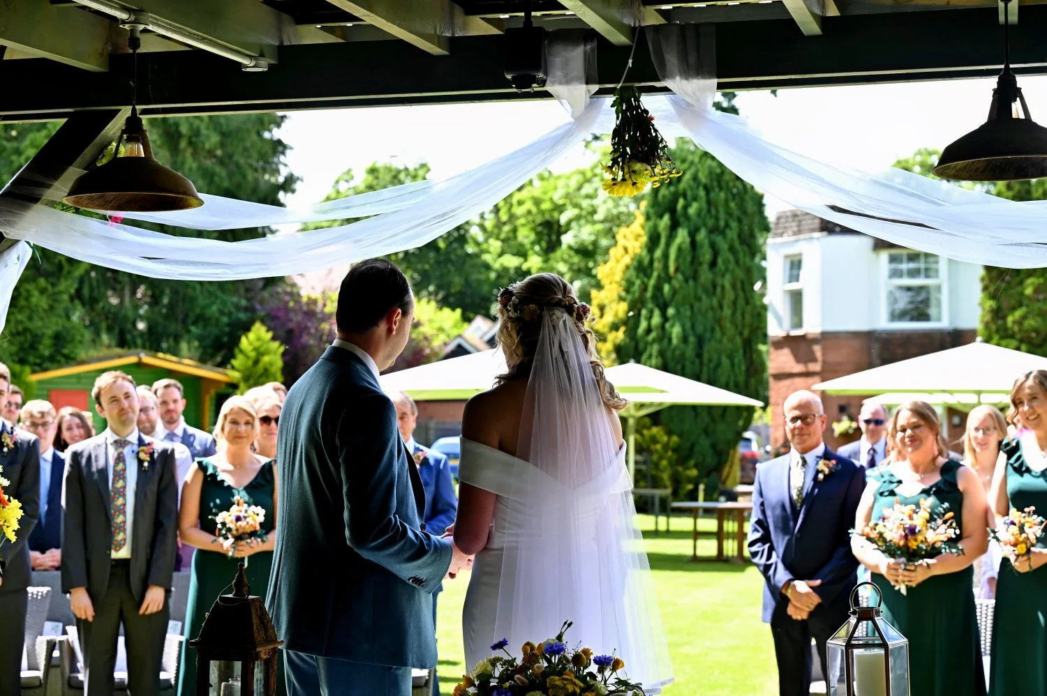 Bride and groom outdoor wedding ceremony under draped pergola, guests watching, flower crown and veil, summer wedding photography Southampton