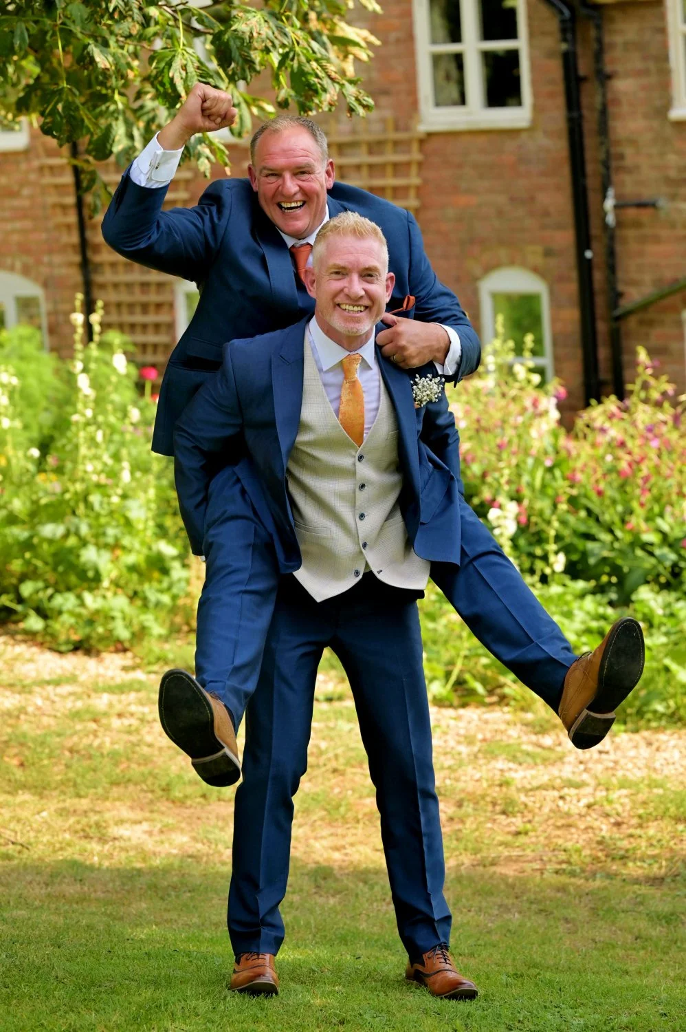 Groom and best man celebrating with a piggyback at a farm wedding in Leicestershire — fun candid wedding photography by Tasha Boorman, Leicestershire wedding photographer