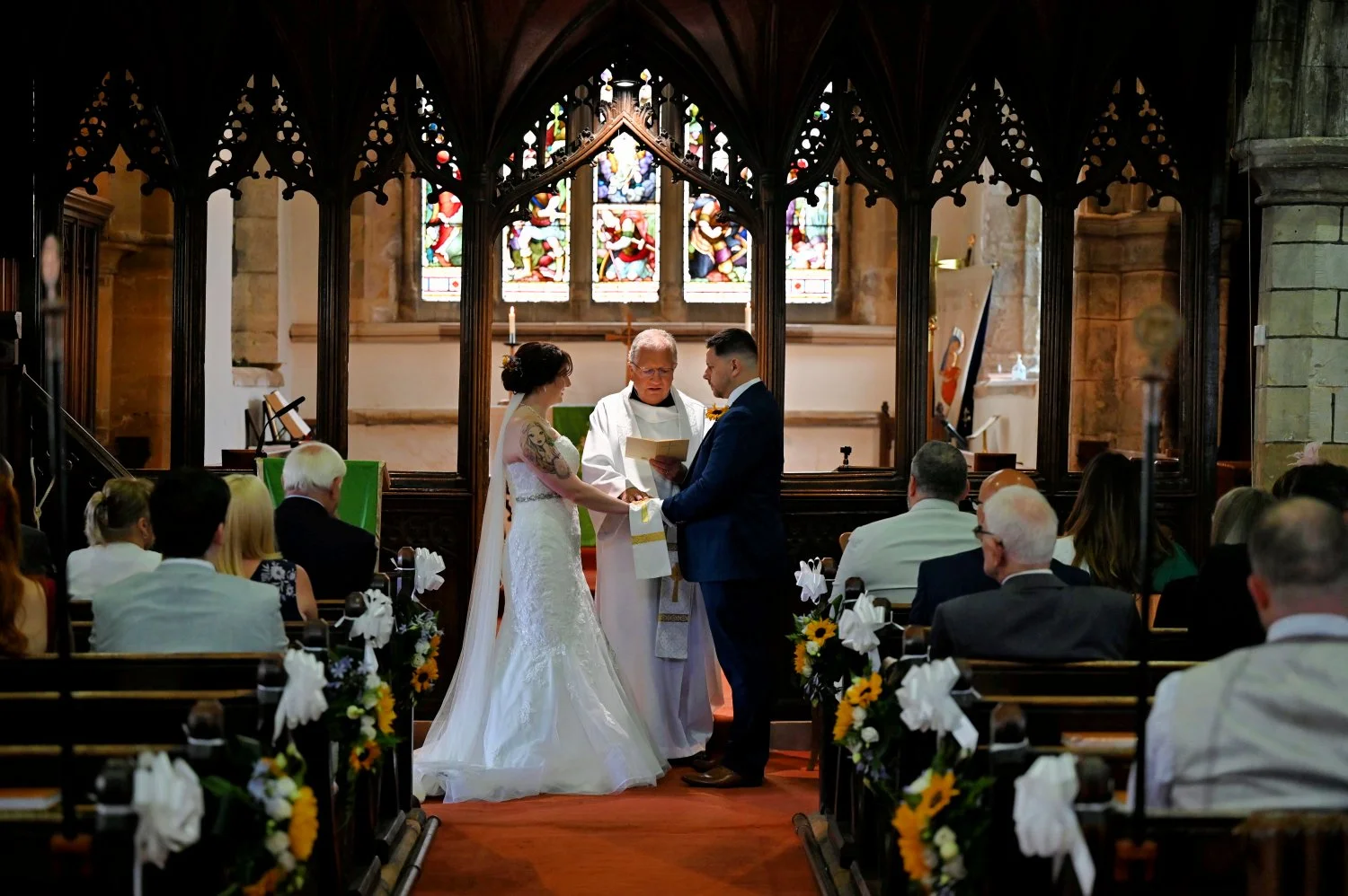 Bride and groom exchanging vows at the altar of a stunning gothic church in Doncaster with beautiful stained glass windows — documentary church wedding photography by Tasha Boorman, Doncaster wedding photographer