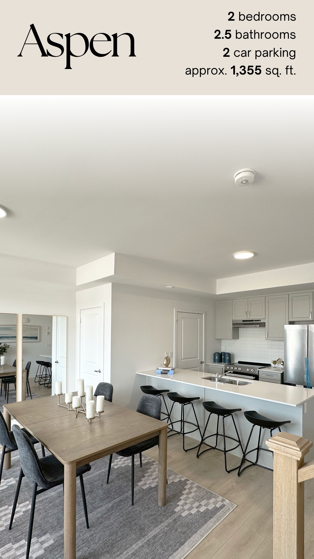Interior view of a modern, white kitchen with a breakfast bar, black bar stools, a dining table with chairs, and decorative candles on the table, with a dining area in the background.