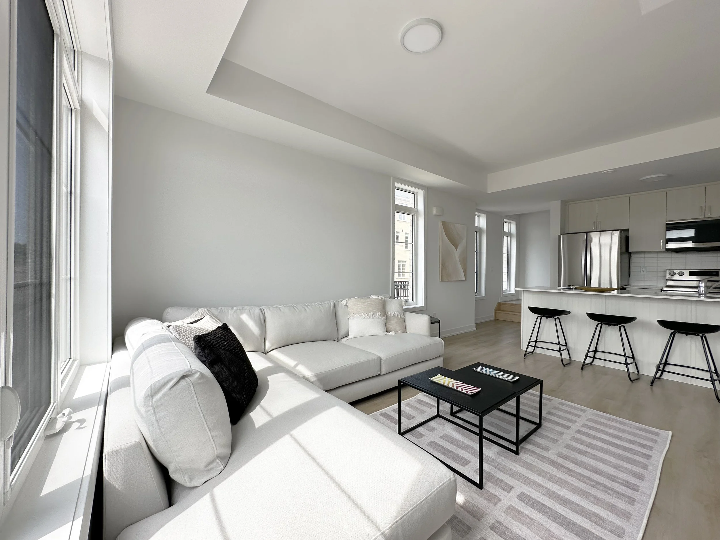Bright living room with white sofa, black coffee table, striped rug, and large windows in a modern apartment.