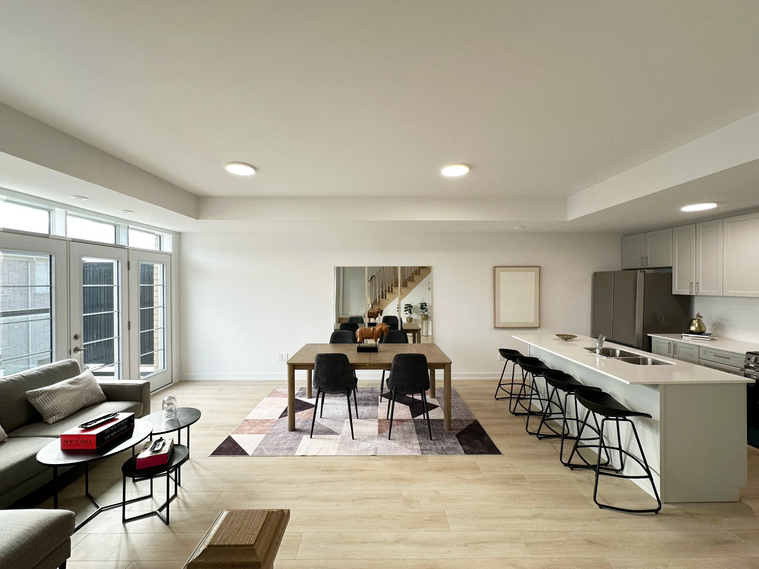Open-concept living room and kitchen with dining area, large windows, and modern furniture.